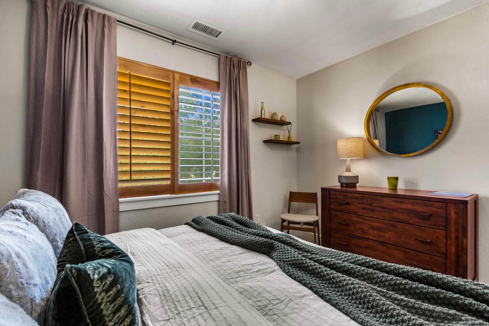Your peaceful retreat awaits with a plush bed, elegant wood furnishings, and soft natural light streaming through plantation shutters—perfect for unwinding after your adventures.