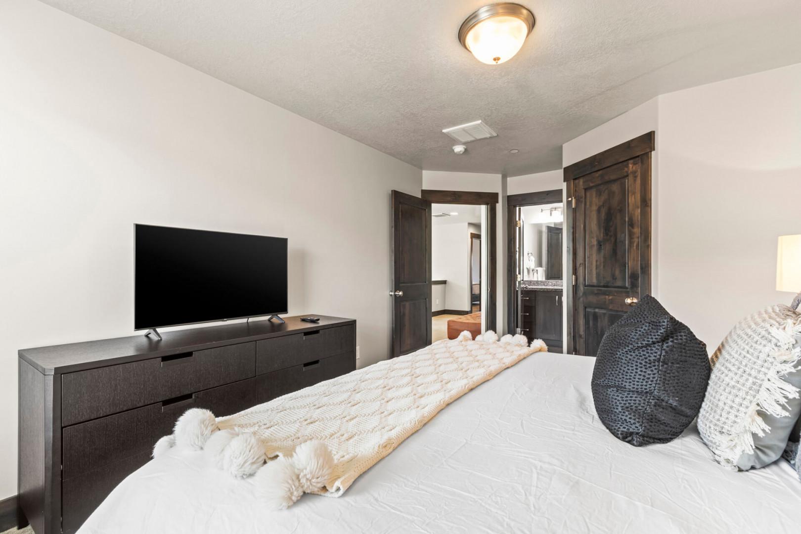 Unwind in your peaceful bedroom with plush bedding, modern TV, and stylish storage for a perfect night's rest.