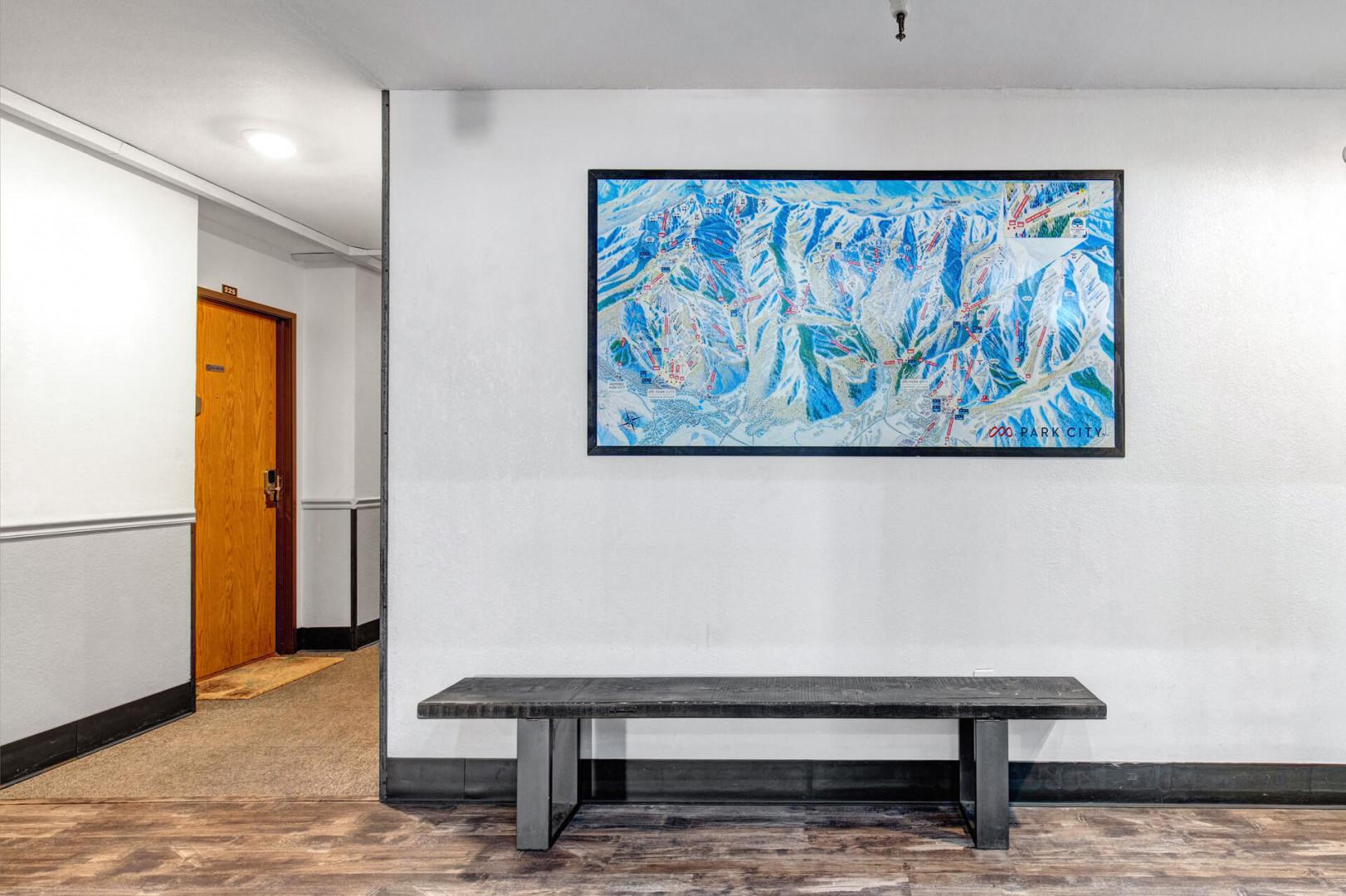 A welcoming entrance hallway features clean white walls and a sleek bench for your convenience. A framed ski trail map adds character to the space, setting the tone for mountain adventures ahead.