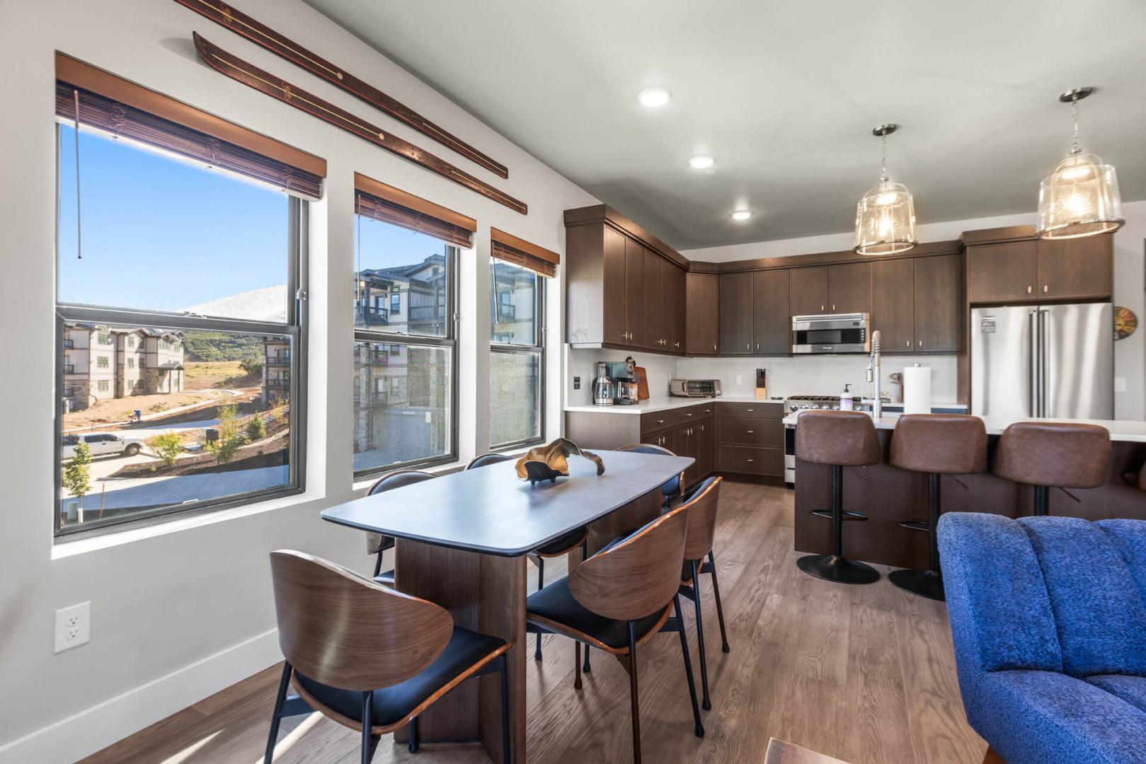 Settle into your open-concept space where modern meets cozy. Enjoy coffee at the sleek dining table, whip up a meal in your fully equipped kitchen, or relax on the plush blue sofa as natural light floods in through expansive windows.