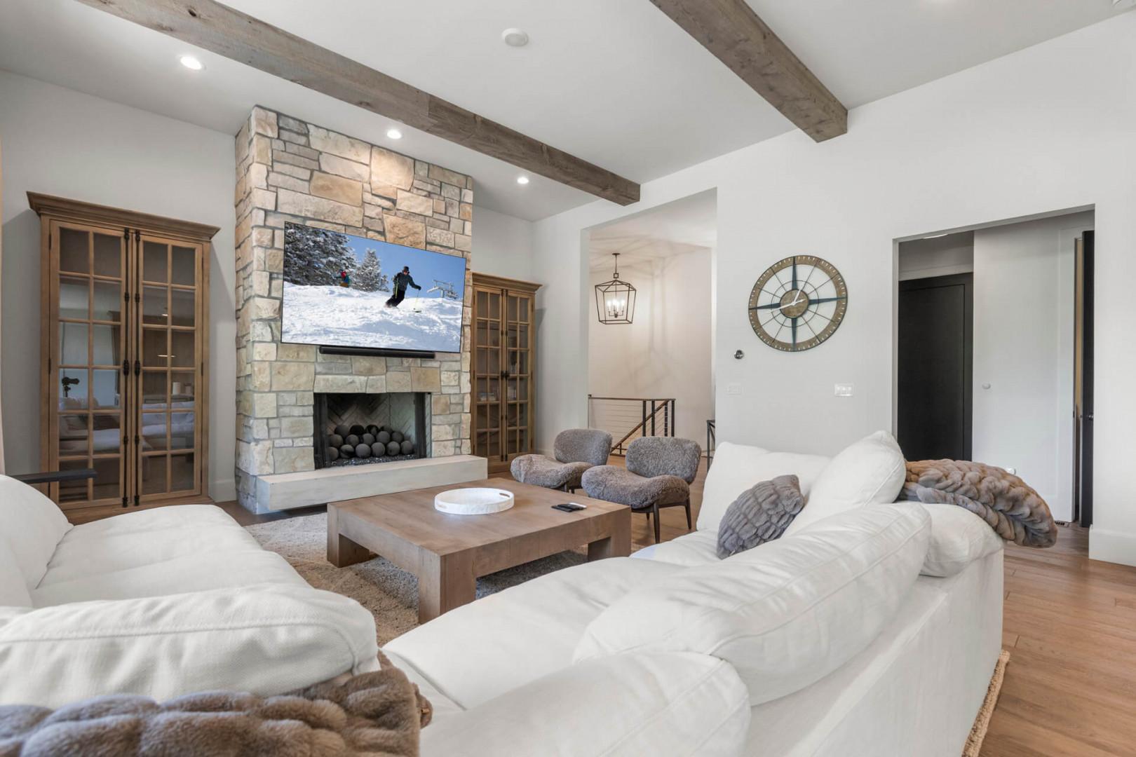Sink into plush seating in your elegant living room, warmed by a stone fireplace with mountain views on screen. Exposed beams and rich wood accents create your perfect après-ski retreat.