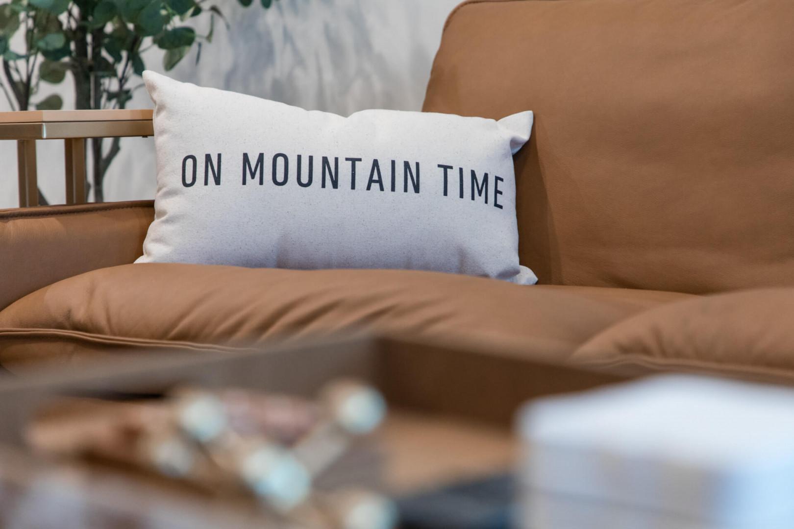 Sink into your cozy sofa where the playful 'On Mountain Time' pillow reminds you to slow down and savor each peaceful moment.