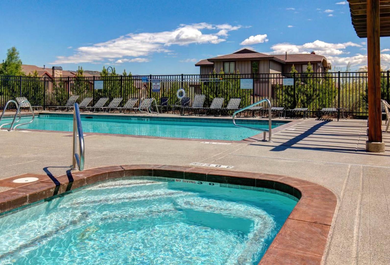 A sparkling hot tub and swimming pool await under clear blue skies, lined with lounge chairs for your ultimate relaxation and sun-soaked poolside moments.