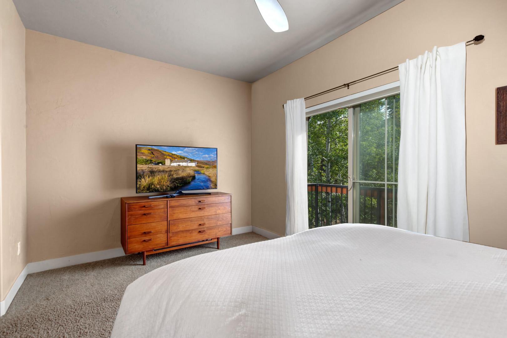 Your peaceful bedroom retreat features a plush bed, smart TV for entertainment, and a window framing lush greenery—perfect for tranquil mornings and restful nights in your home away from home.