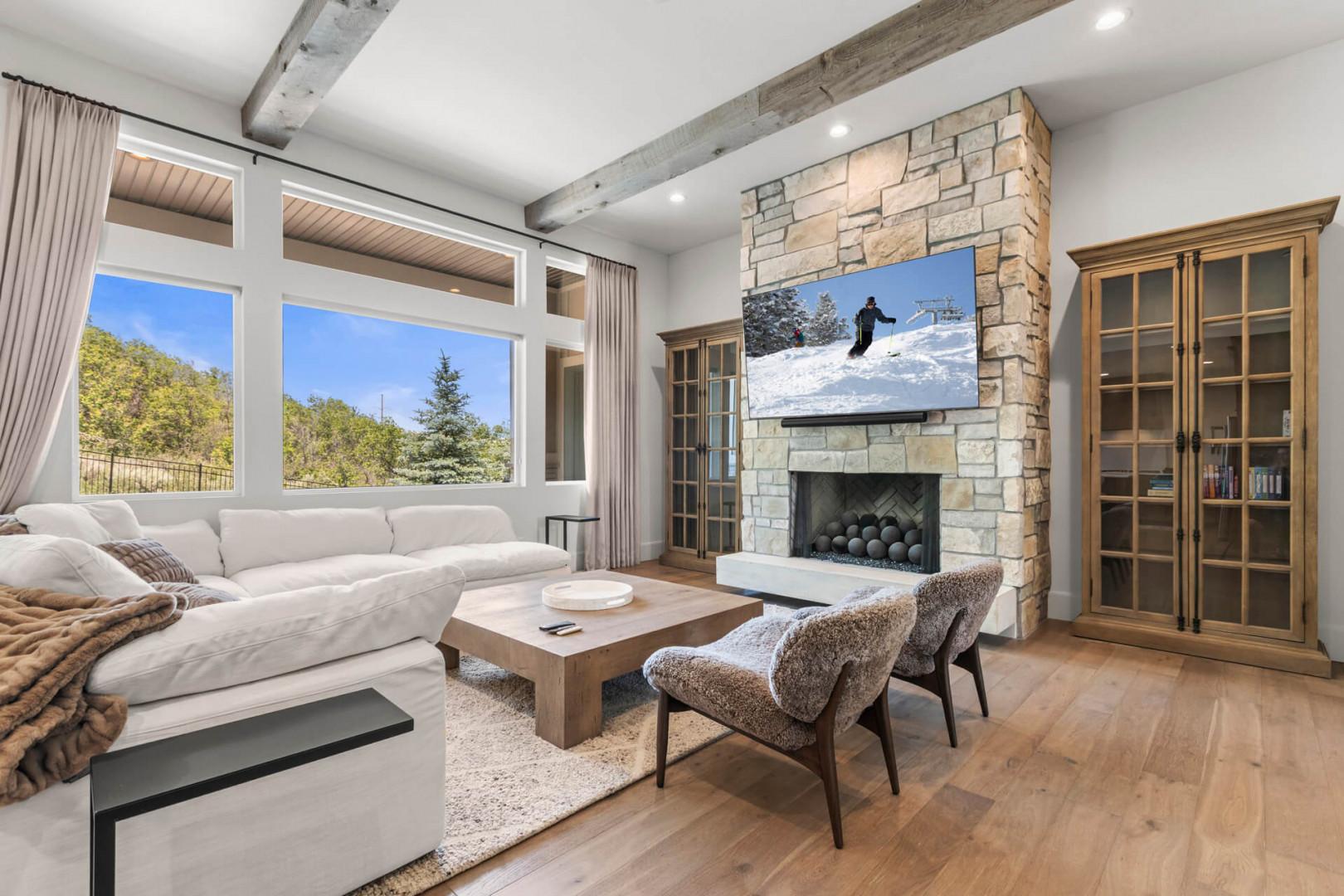 Cozy main level living room with stunning natural light, exposed beams, and a stone fireplace where you can unwind after mountain adventures.