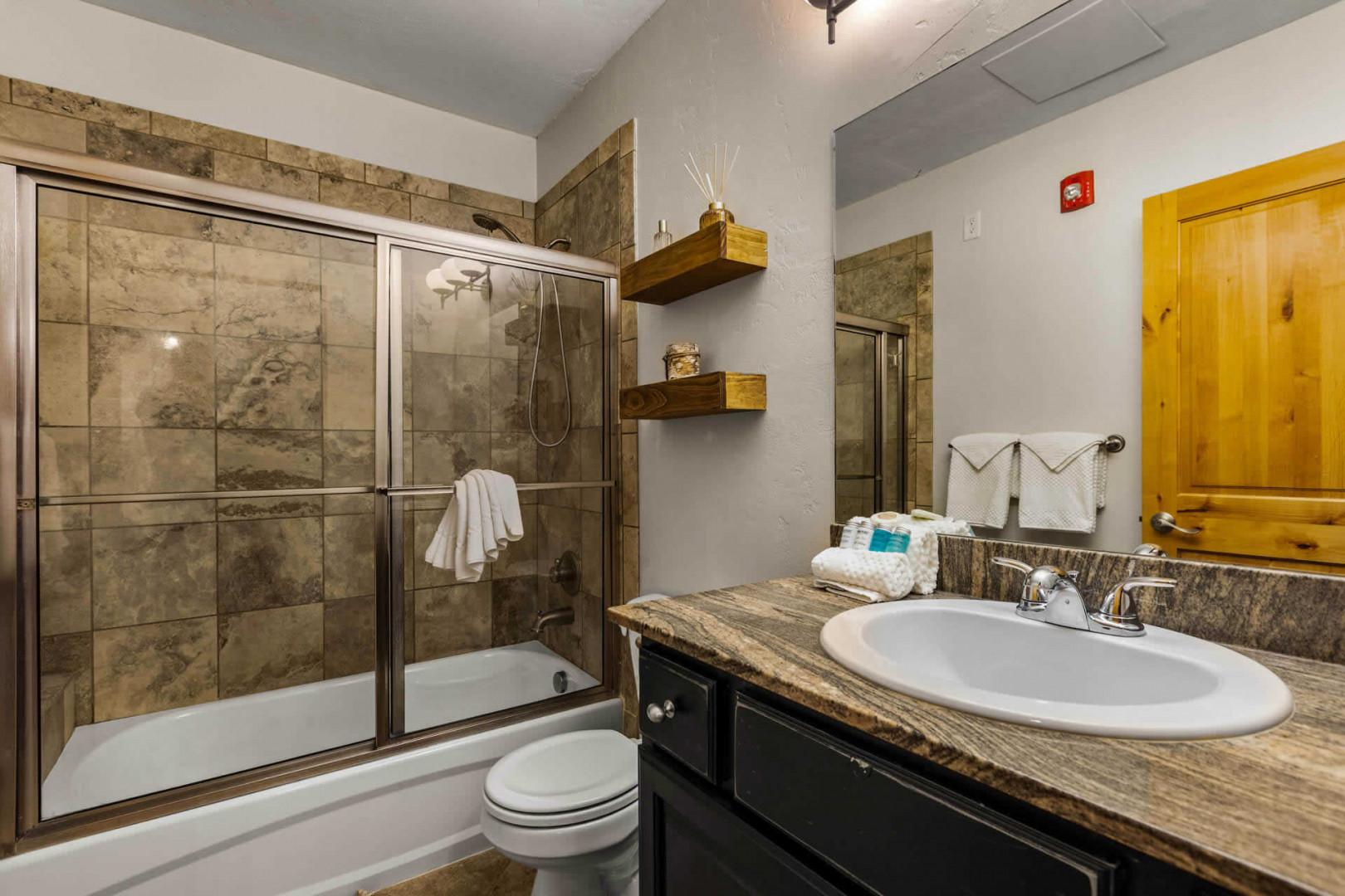 Your private bathroom offers a spacious walk-in shower with glass doors, plush towels, and warm rustic accents that create a relaxing retreat after your adventures.