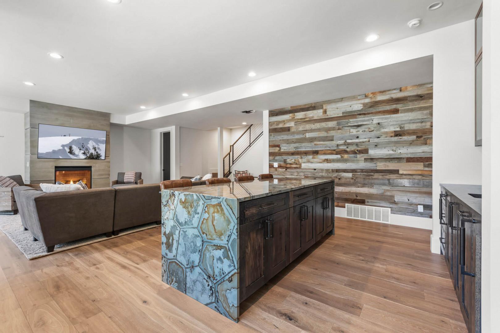 Unwind in your open-concept living space where rustic reclaimed wood meets modern comfort, complete with a cozy fireplace, sleek island with striking stone detail, and warm hardwood floors inviting you to relax.