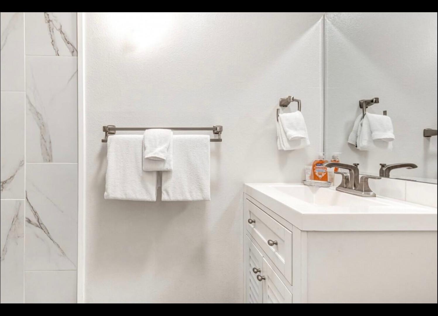 Pamper yourself in this pristine bathroom featuring elegant marble-look tiles and plush white towels awaiting your arrival.