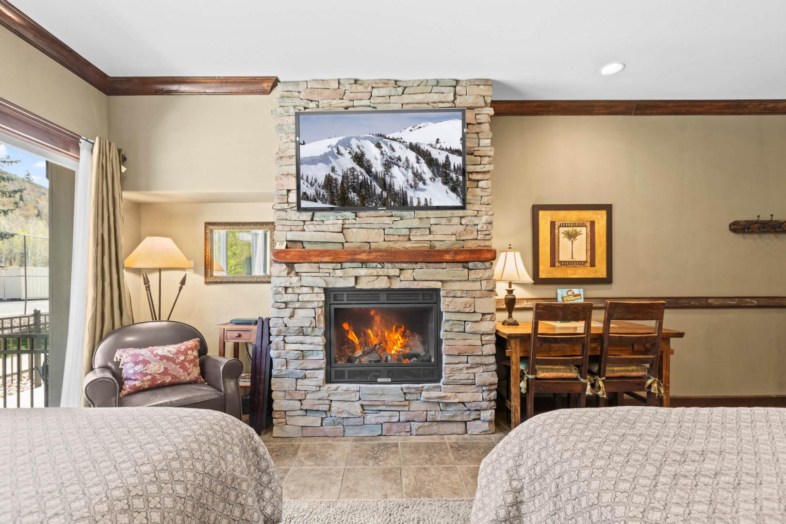 Unwind in your cozy living space with a crackling fireplace and mountain views on the TV, perfect for relaxing après-ski evenings.