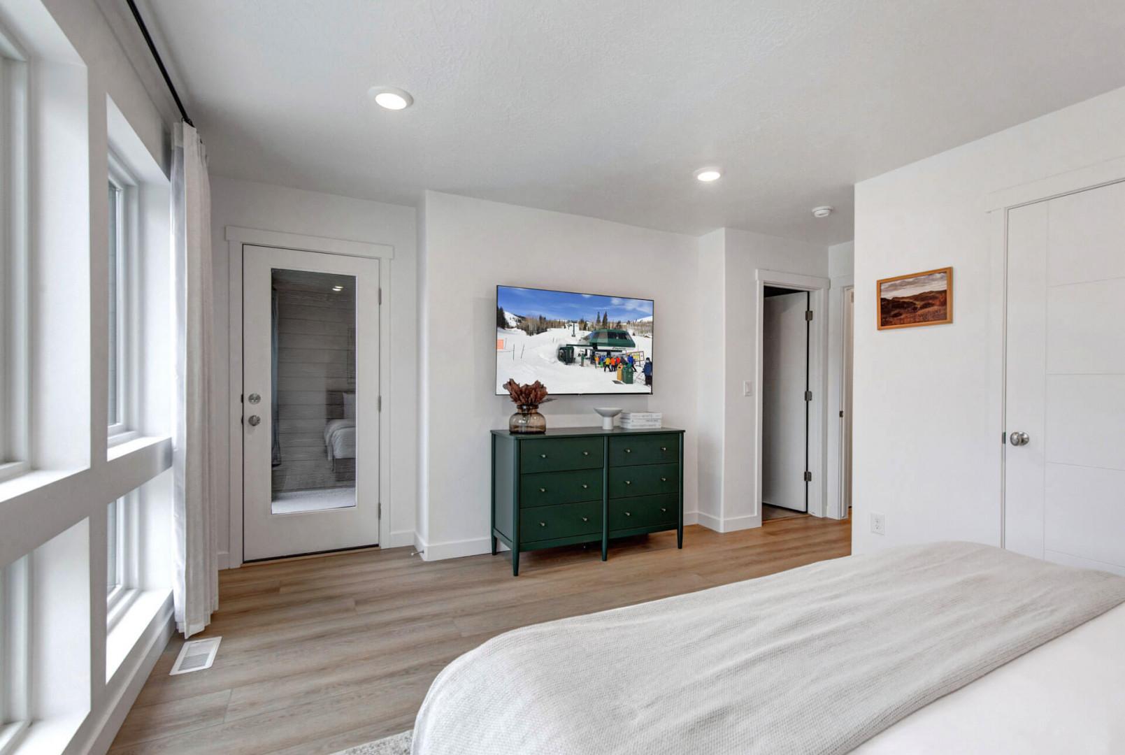 Relax in your spacious bedroom featuring a smart TV, elegant green dresser, and glass door leading to your private ensuite bathroom.