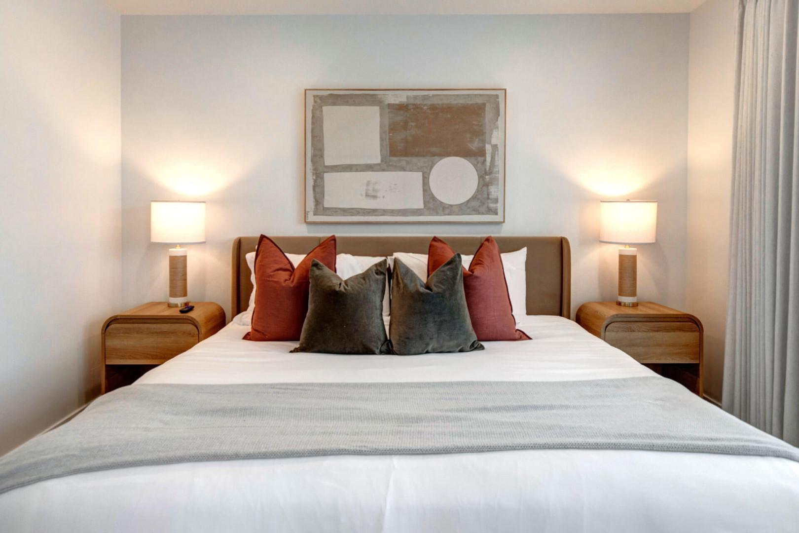 Sink into this plush bed with crisp linens and vibrant pillows, where warm bedside lighting creates your perfect retreat.