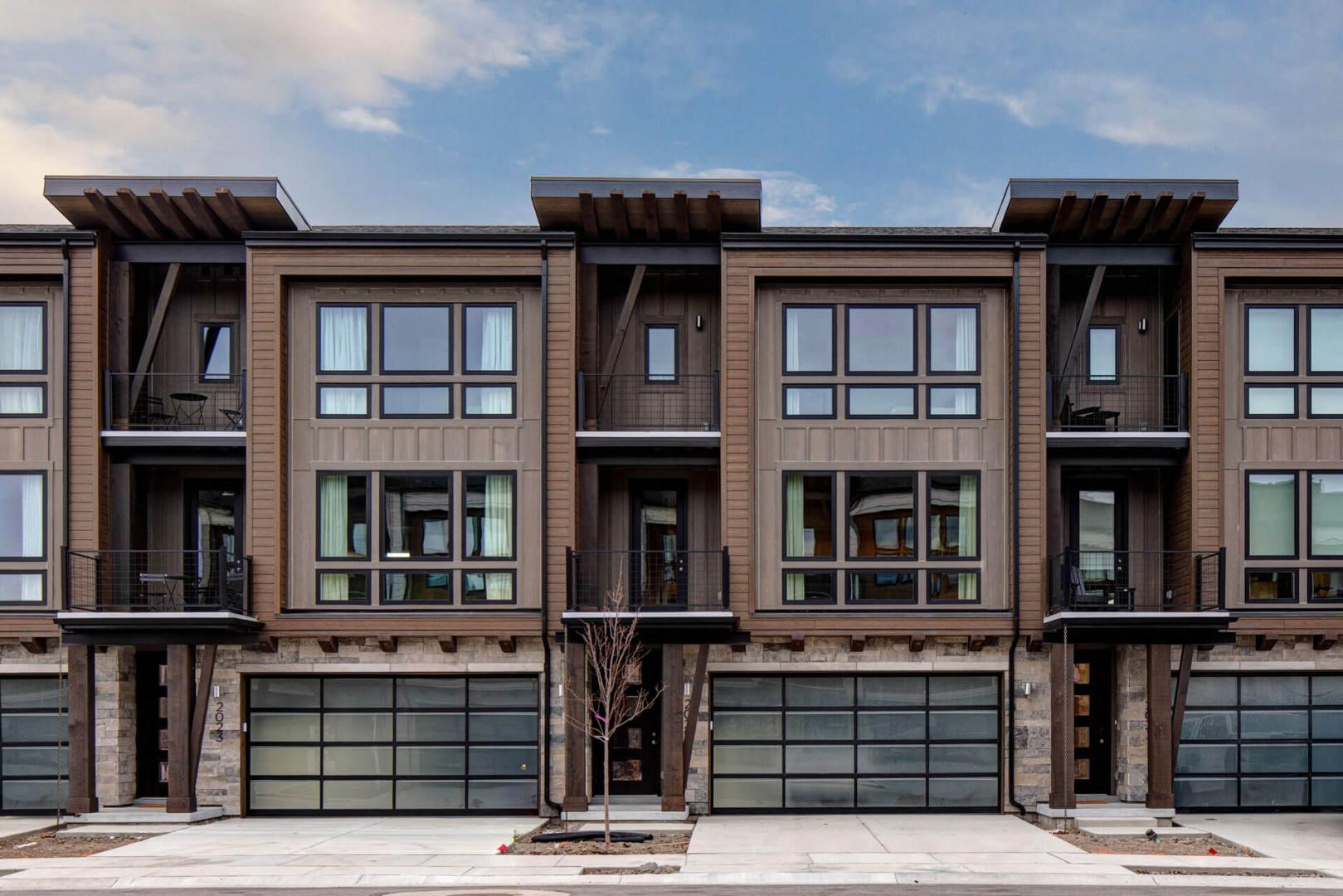 Modern townhomes with stone and wood exterior featuring private garages and contemporary design.