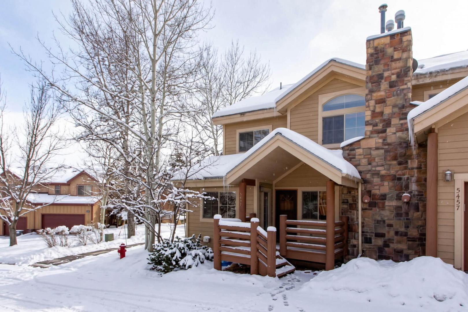 This inviting mountain retreat features a distinctive stone fireplace and cozy covered entry, blanketed in fresh winter snow and surrounded by peaceful neighborhood views.