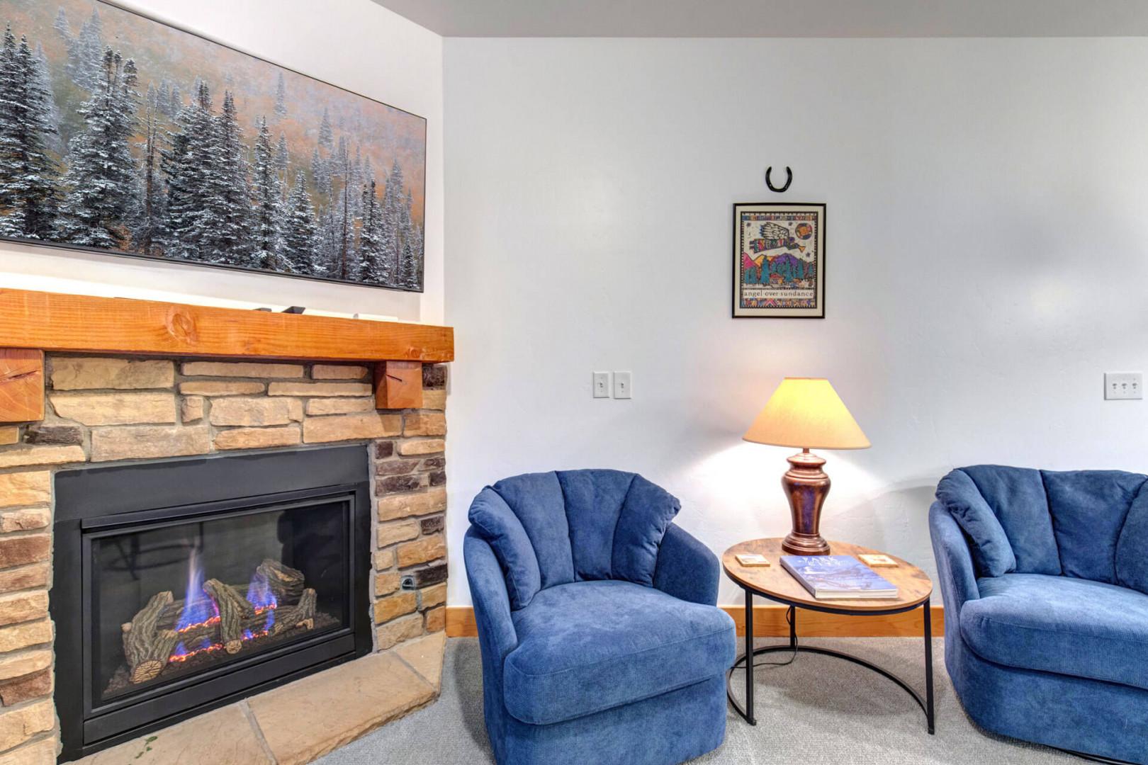 Sink into plush blue chairs by your cozy stone fireplace, where warm light creates the perfect evening retreat.