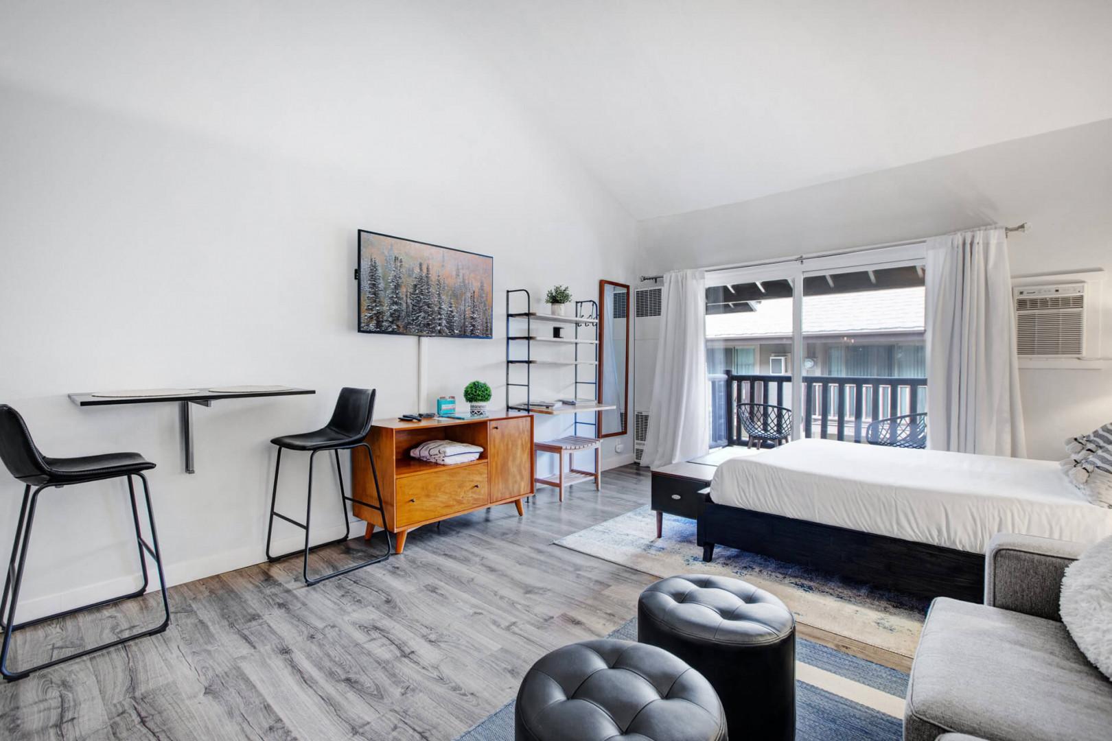 Your stylish studio blends comfort and functionality with modern furnishings, mountain artwork, and natural light streaming through your private balcony.