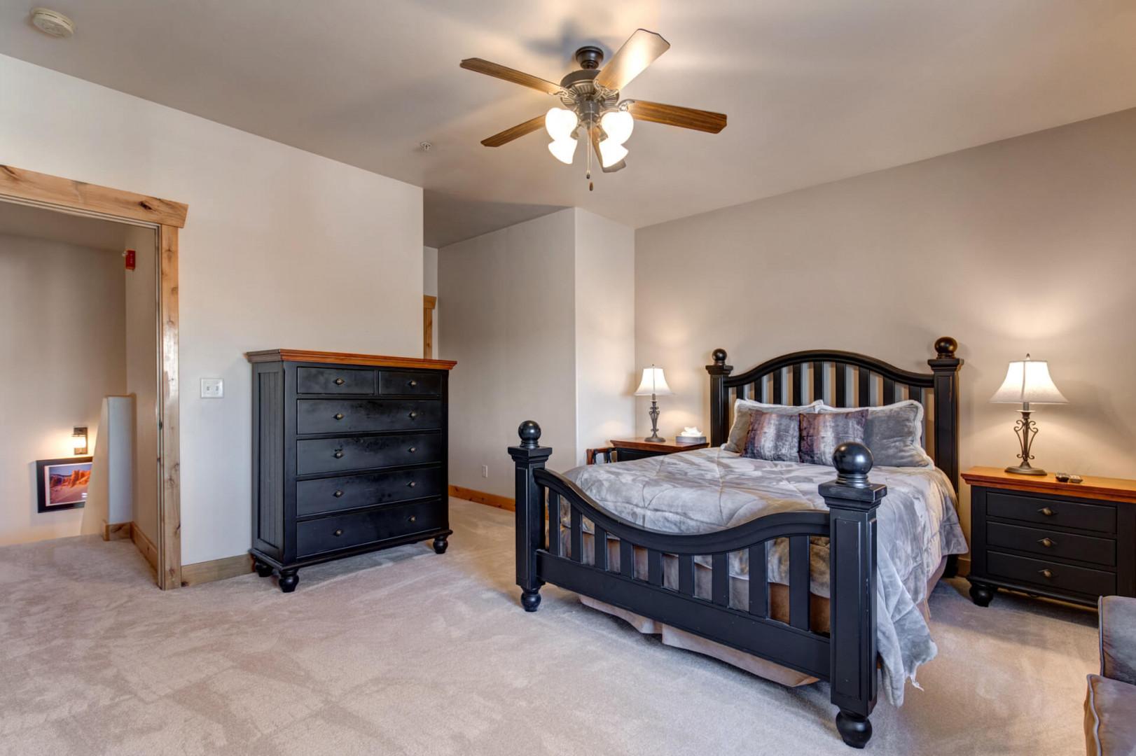 Drift off to sleep in this spacious master bedroom featuring elegant dark wood furniture, plush bedding, and gentle ceiling fan breezes for your comfort.