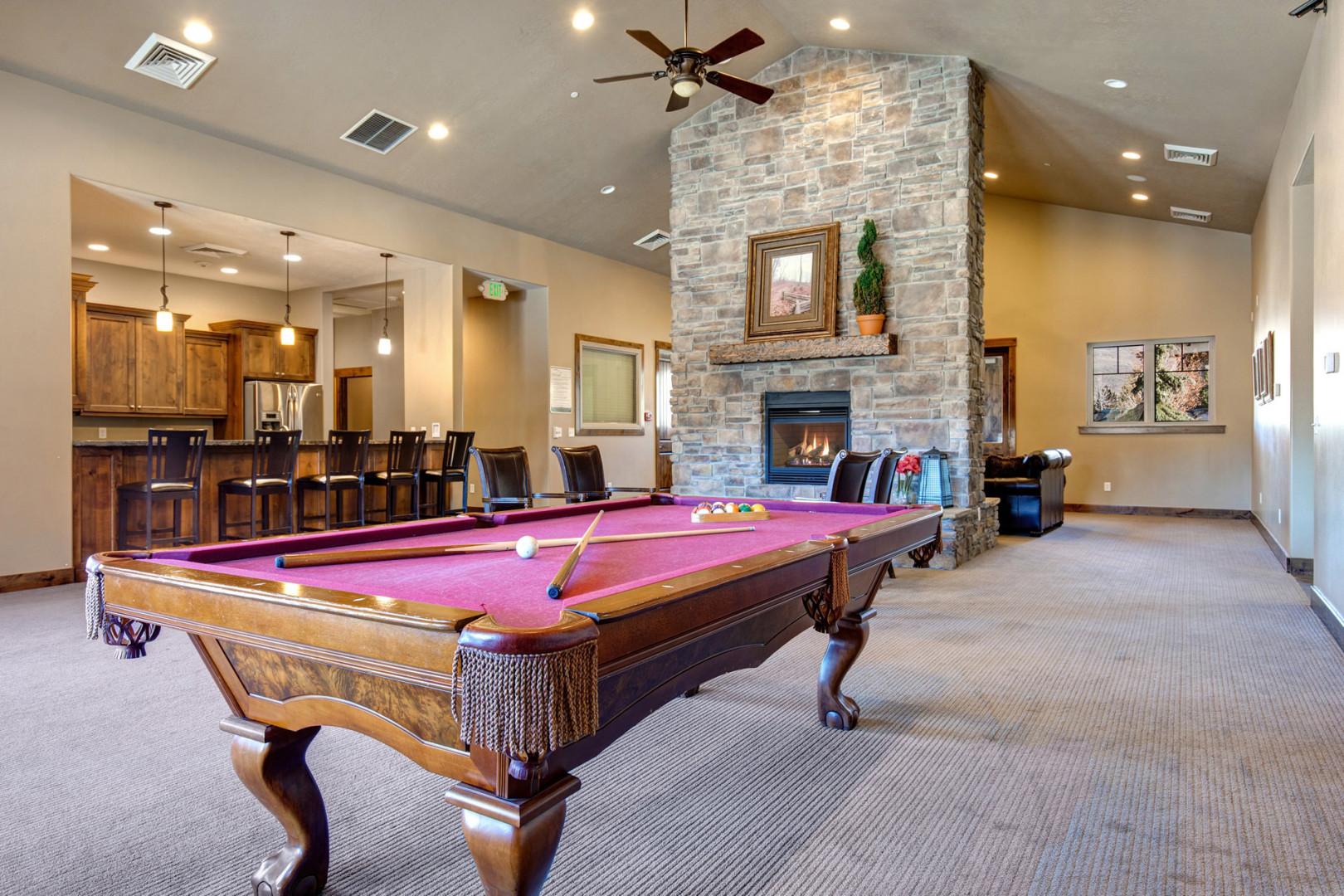 Step into your game room where a classic billiard table awaits beneath soaring ceilings, with a cozy stone fireplace creating the perfect atmosphere for friendly competition and memorable evenings together.
