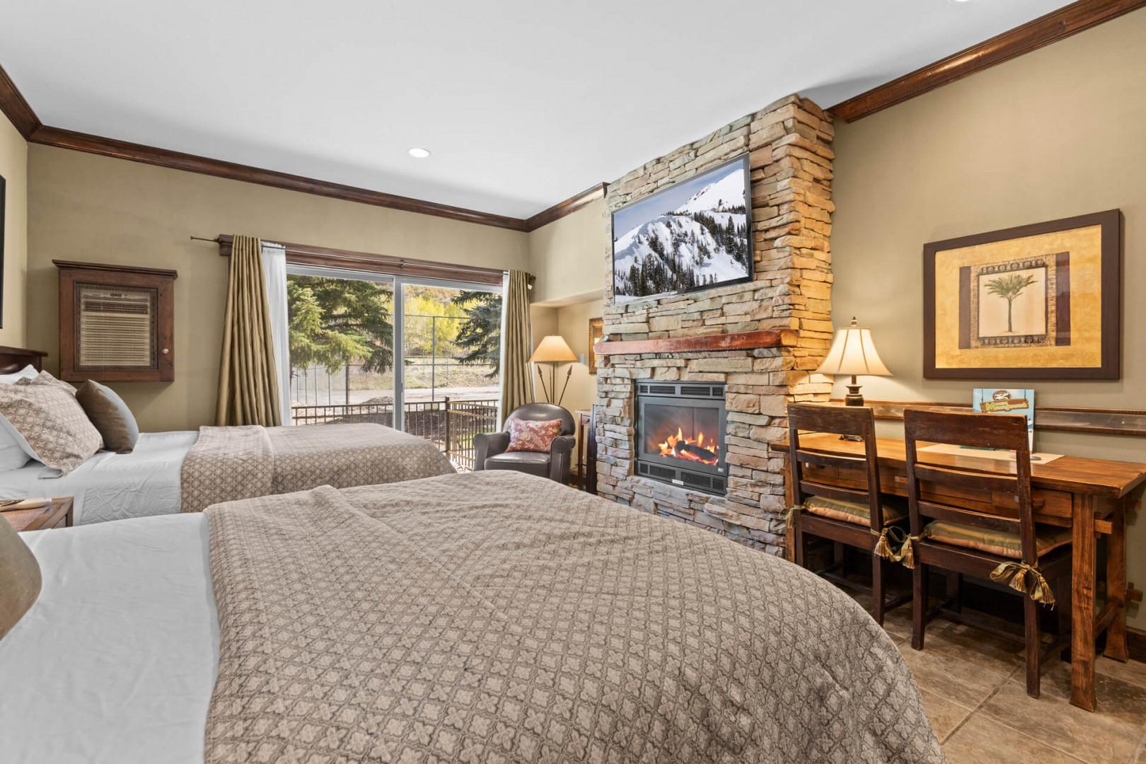 Unwind in your cozy mountain retreat with two plush beds, a stone fireplace, and a workspace overlooking serene forest views—your perfect alpine escape.