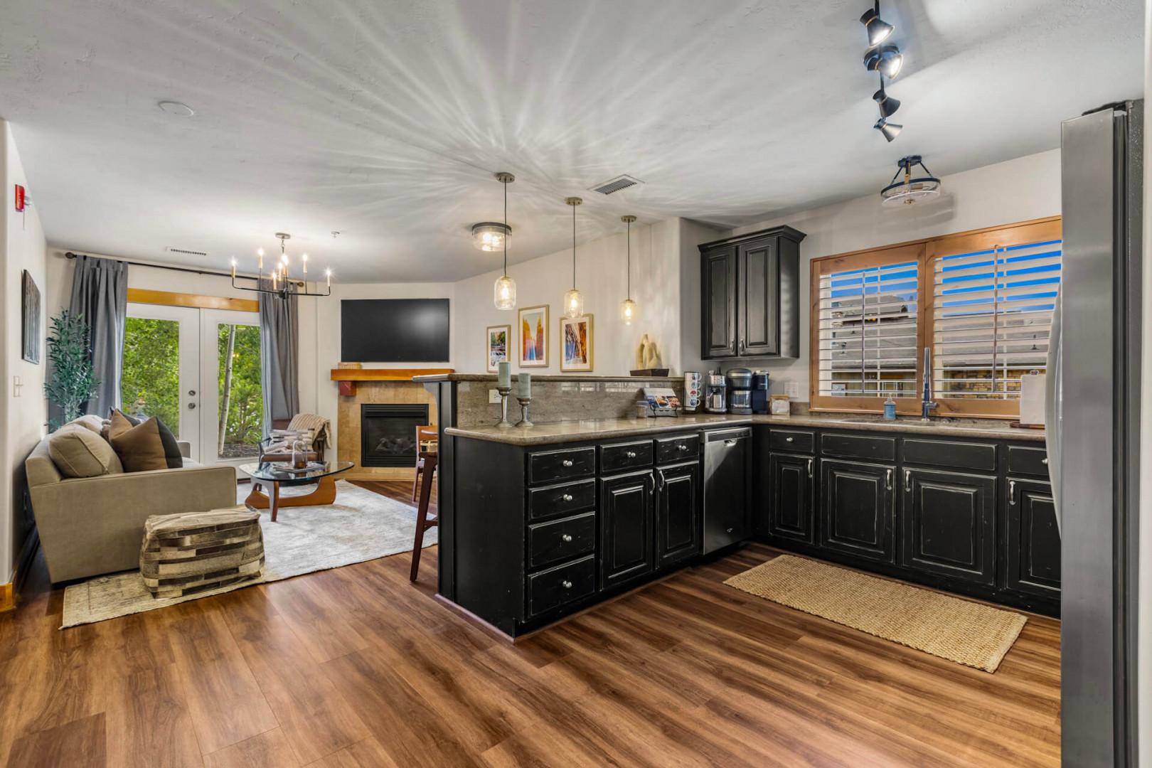 Your stylish open-concept living space features a fully-equipped kitchen with sleek black cabinetry and modern appliances flowing seamlessly into a cozy lounge area with a warm fireplace.