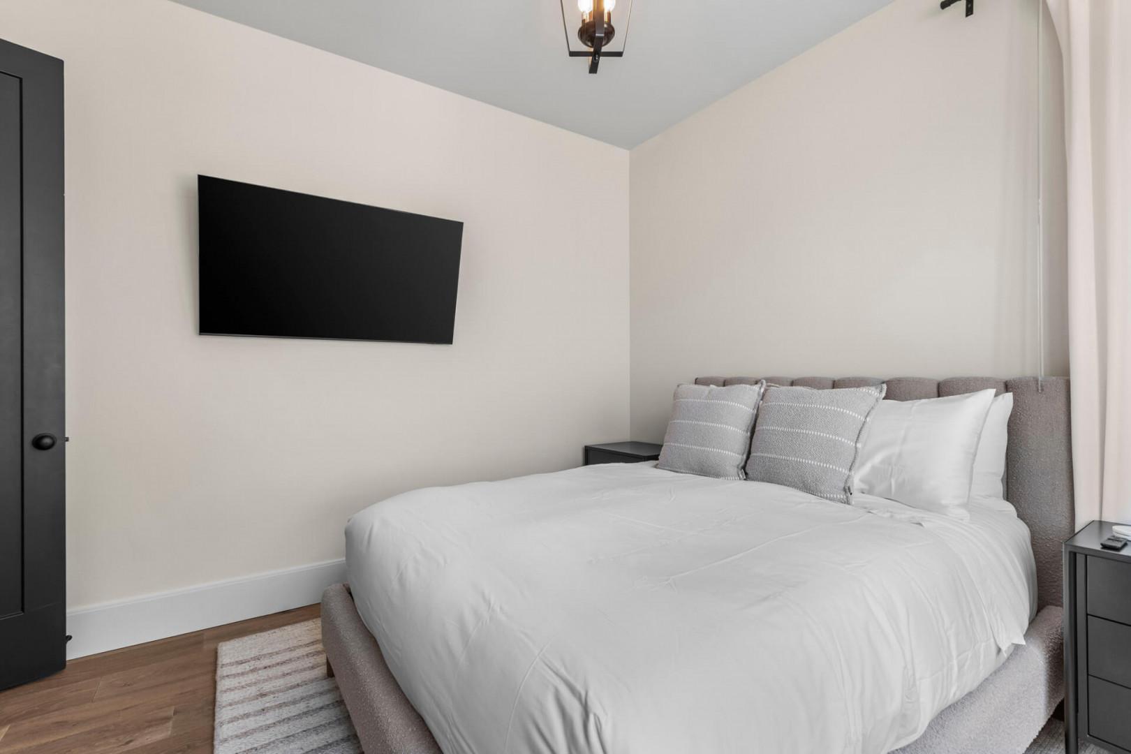 Sink into plush white linens and enjoy your favorite shows on the wall-mounted TV. This serene bedroom offers a peaceful retreat with modern comforts at your fingertips.