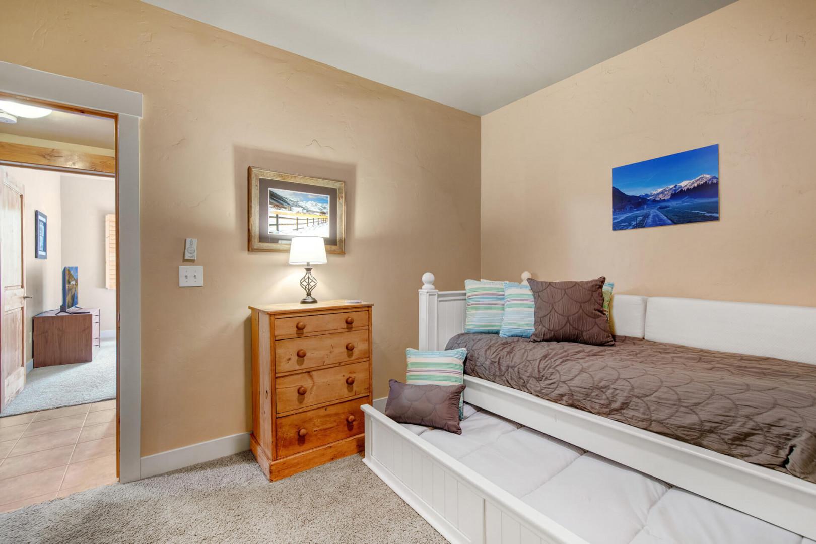 Settle into your cozy bedroom with soft carpeting and a comfortable bed dressed in neutral linens. A classic wooden dresser and mountain artwork create a warm, restful ambiance for peaceful nights.