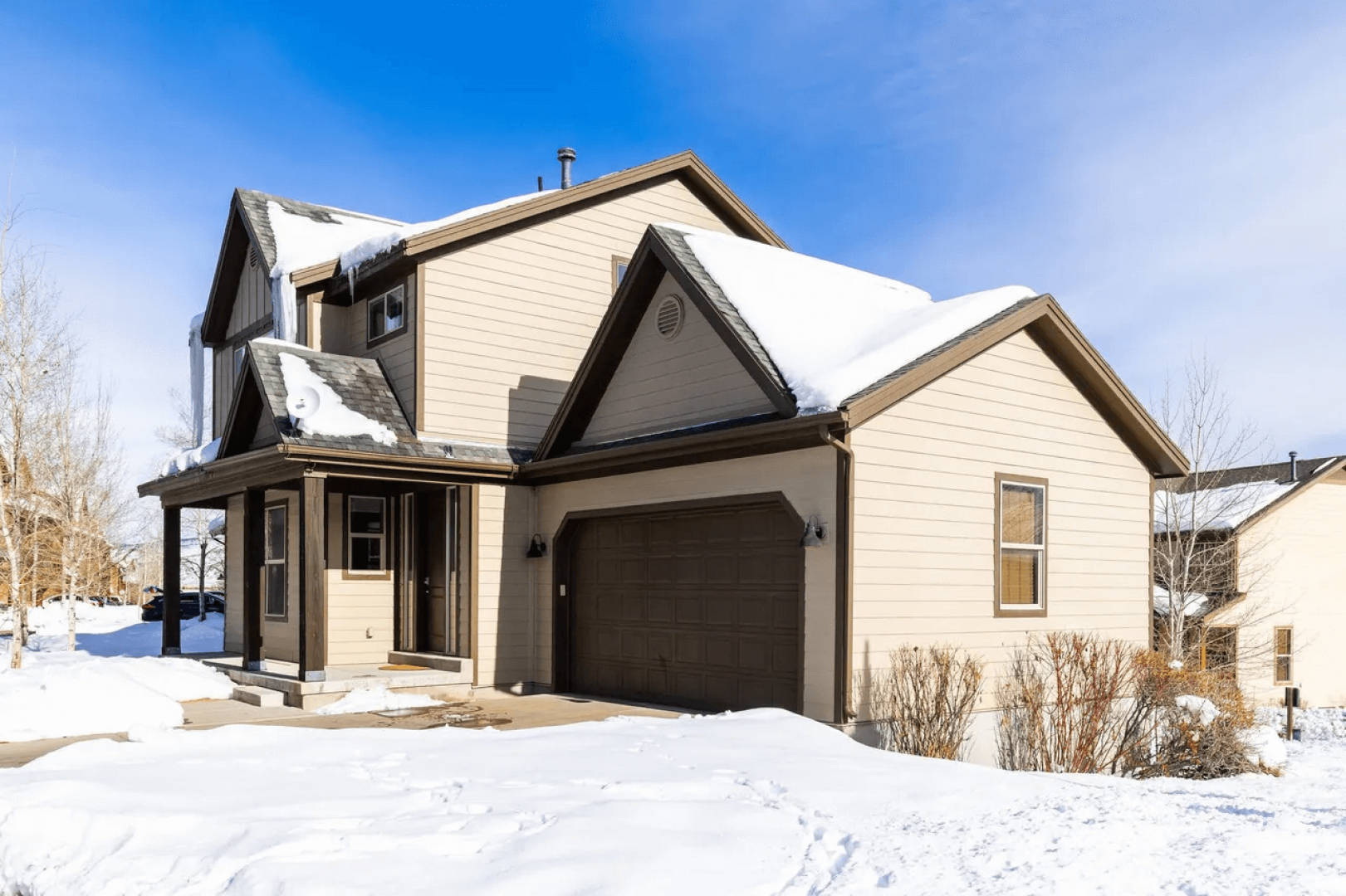 Snow-covered vacation home with attached garage in peaceful residential neighborhood during winter season.