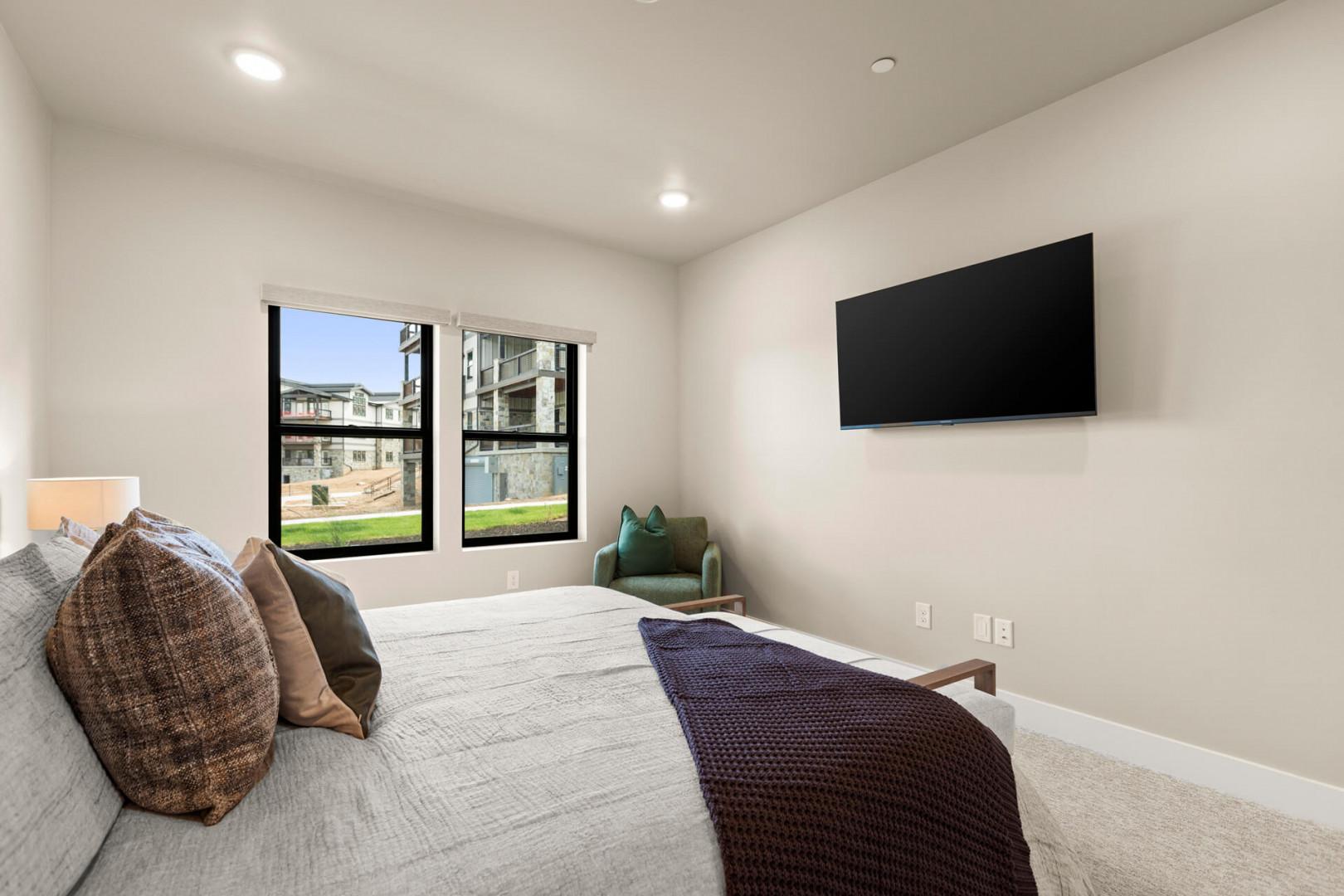 Sink into your plush bed and unwind in this peaceful bedroom, where natural light streams through large windows and a wall-mounted TV awaits your favorite shows.