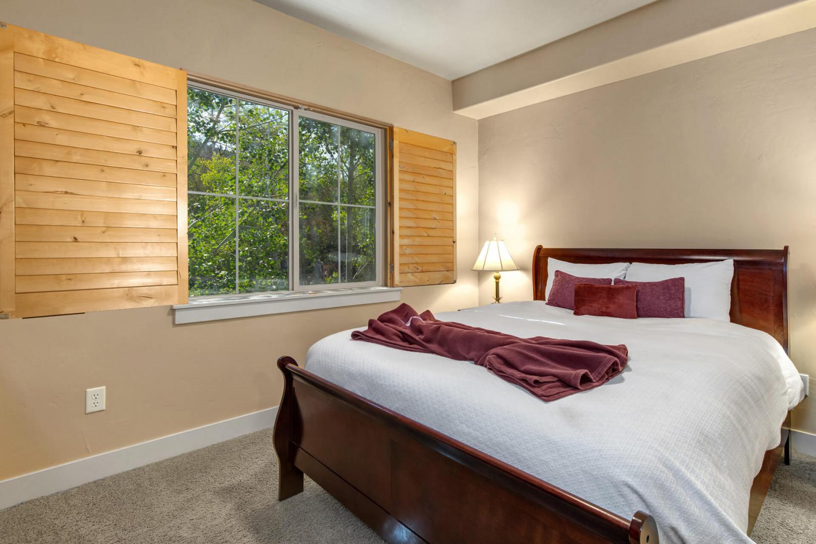 Your tranquil bedroom retreat features a plush bed with crisp linens and warm wood accents, framed by a window showcasing peaceful garden views for restful mornings.