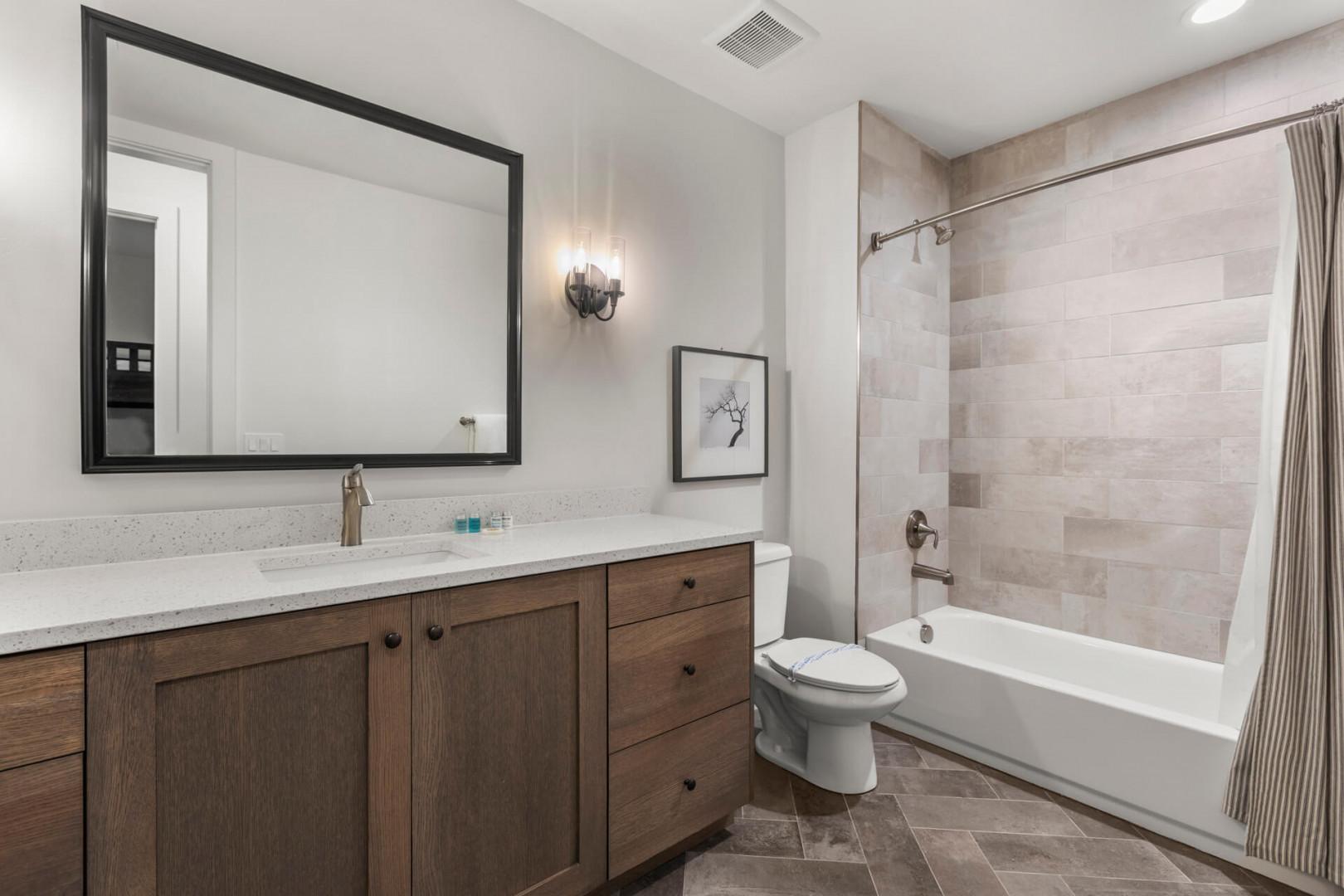 Relax in your spacious bathroom featuring modern finishes, a full tub with stylish tiled surround, and elegant wooden vanity with ample storage for your toiletries.