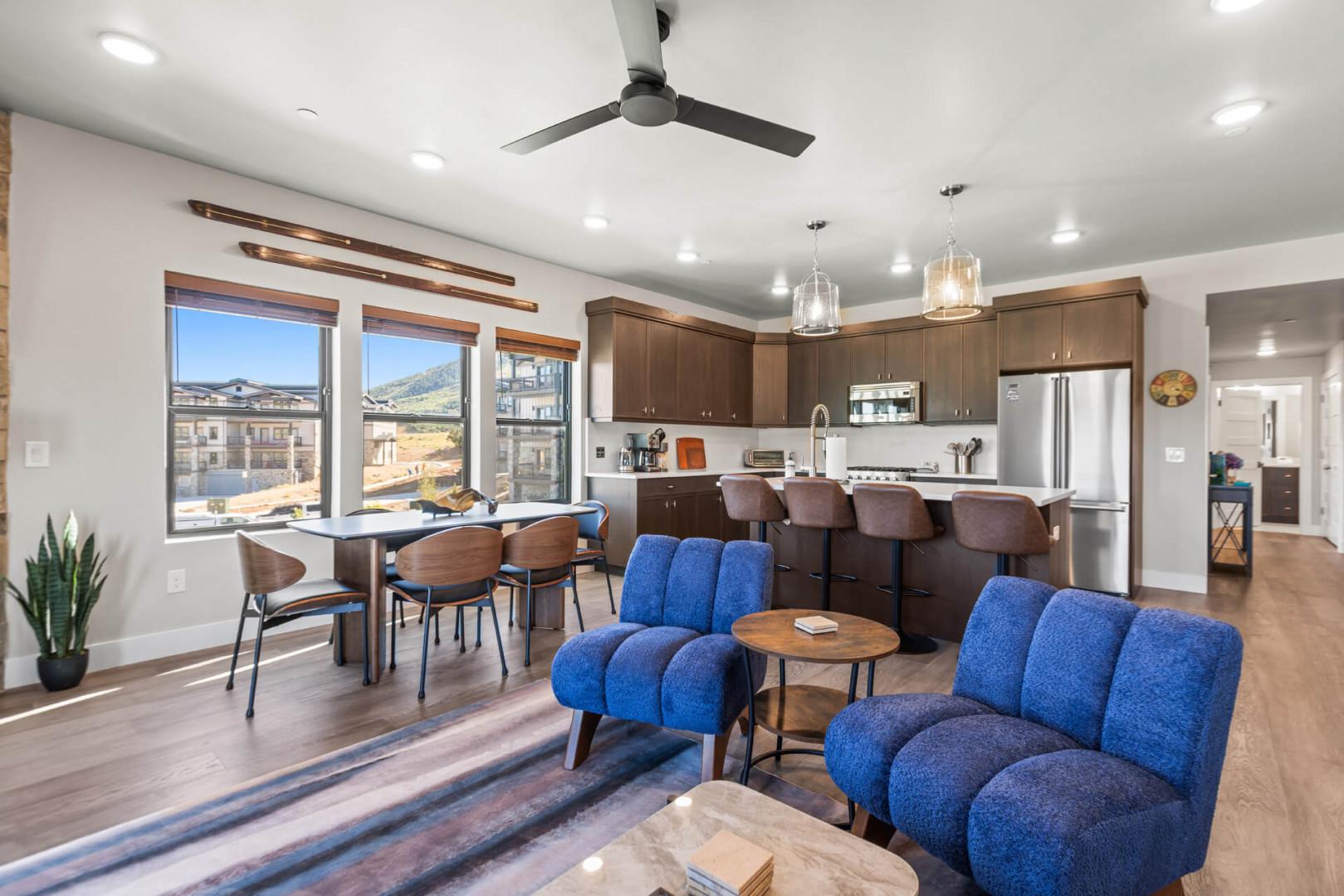 Your open-concept living space blends kitchen, dining, and lounge with modern comfort and natural light. Plush blue seating invites you to relax, while mountain views through large windows frame your stay.