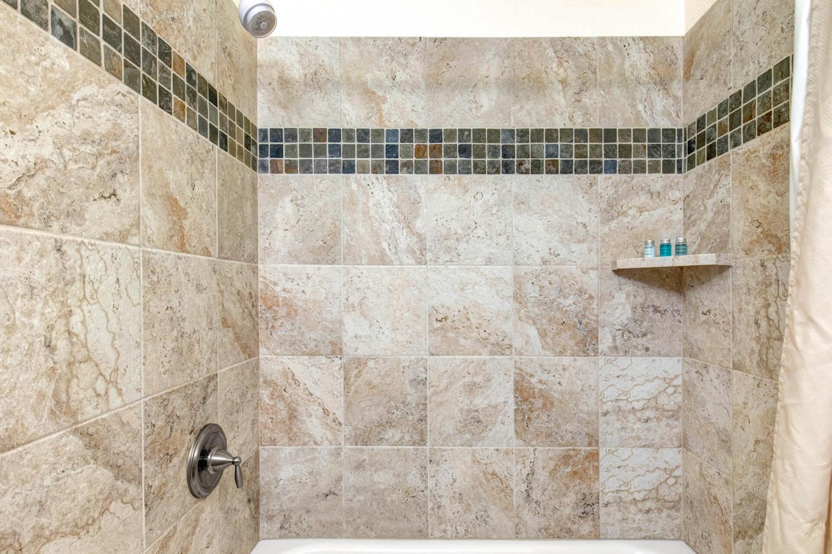 Step into your beautifully tiled walk-in shower with elegant travertine and mosaic accents, stocked with complimentary amenities for your comfort.