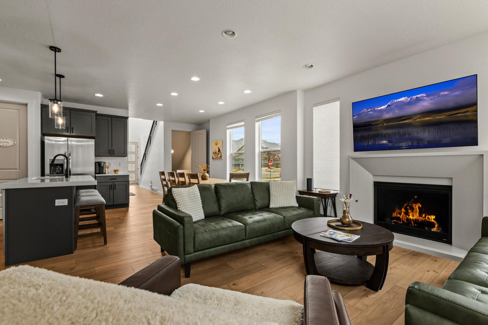 Unwind in your open-concept living space where emerald leather sofas face a crackling fireplace, perfectly positioned for cozy evenings.