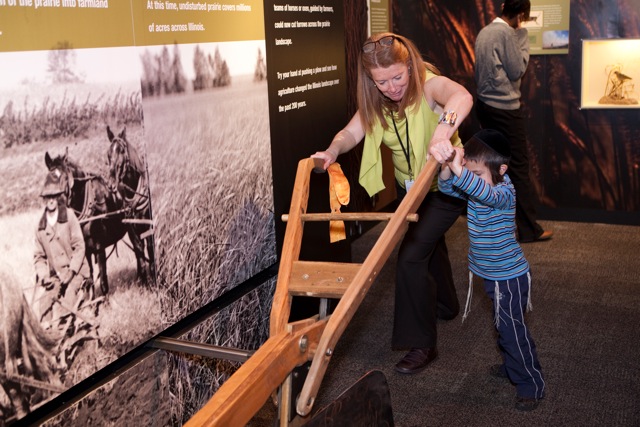 The Peggy Notebaert Nature Museum's President and CEO Deborah Lahey pushes a 19th-century plow replica with an exhibit guest. (Peggy Notebaert Nature Museum)