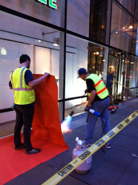 A volunteer uses a blow torch to heat up the sidewalk before laying down vinyl for ‘Color Jam.’ (WBEZ/Robin Amer)