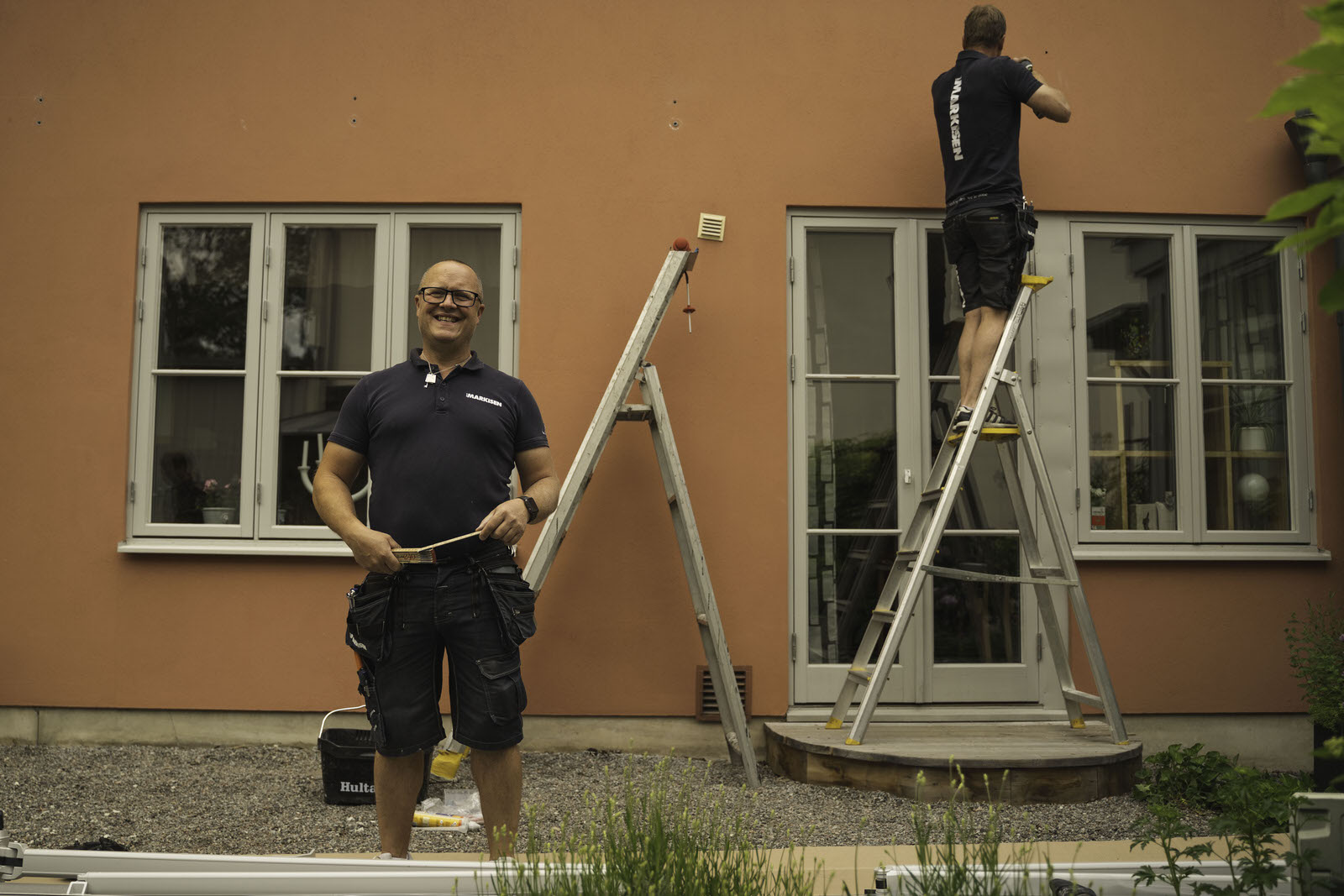 Two tradespeople on ladders painting the outside of a house