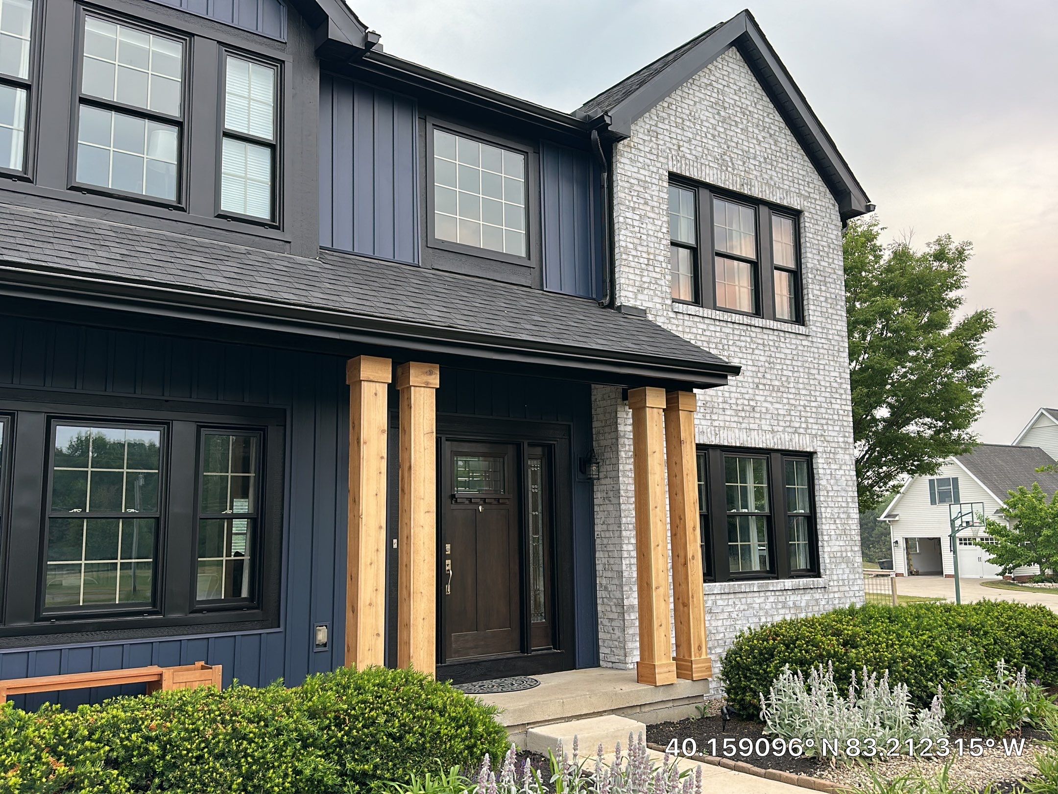Front entry of the renovated home, with natural wood detailing framed by dark siding and light stone