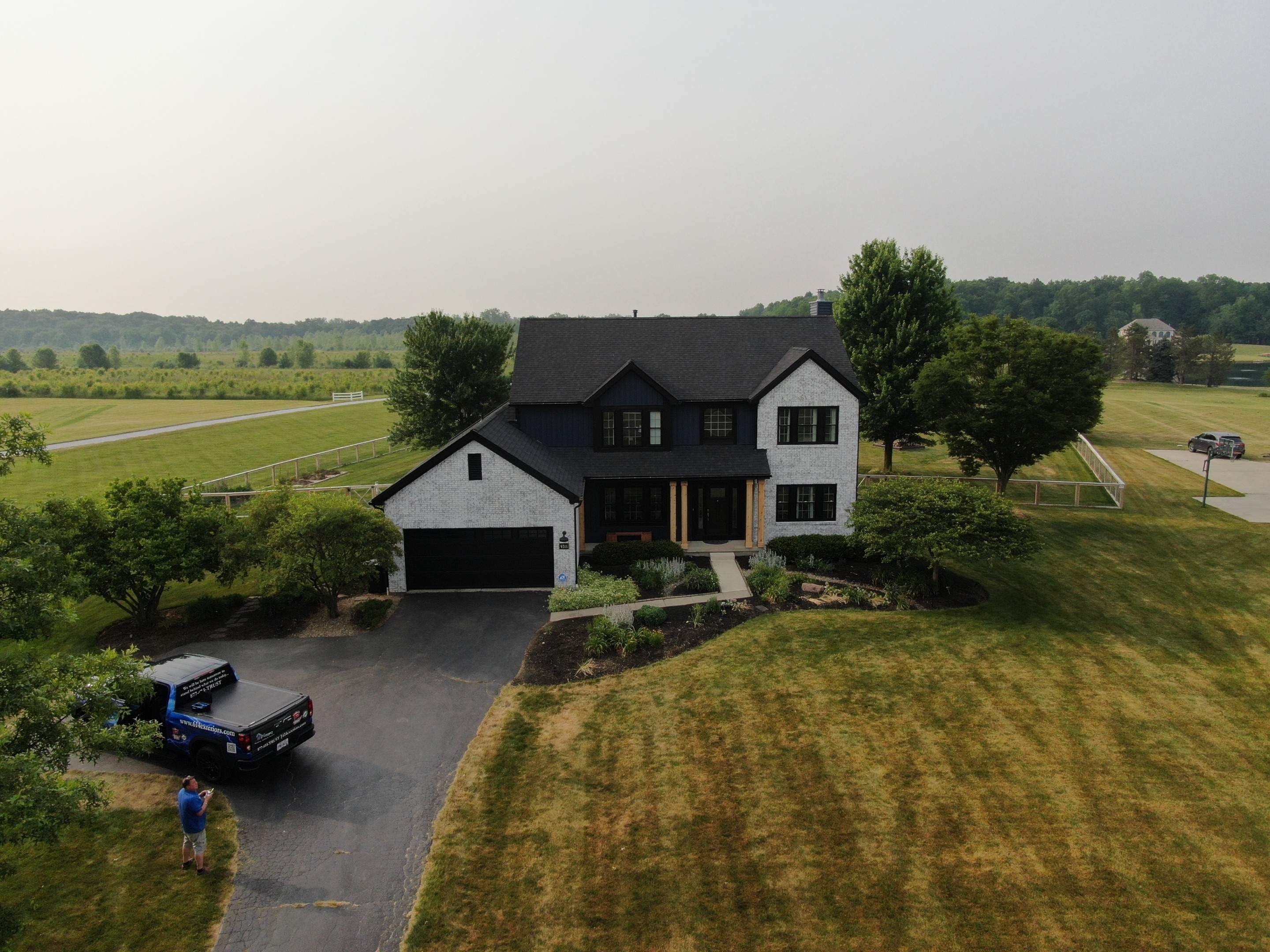 Aerial front view of a two-story Marysville home after exterior renovation, with a dark roof and dark siding against light stone
