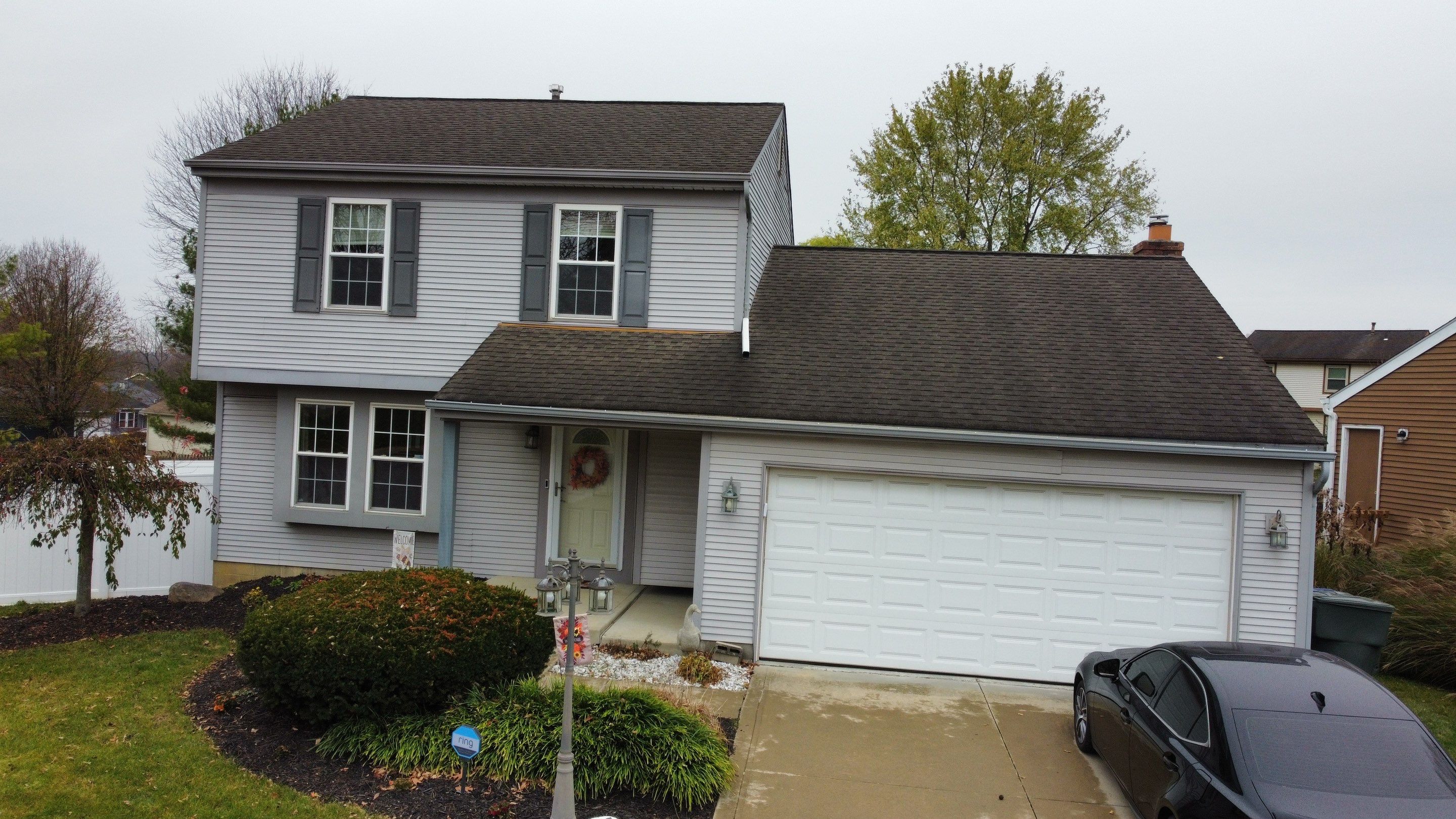 Front of the two-story home before roofing and siding replacement, with white siding and an older dark roof