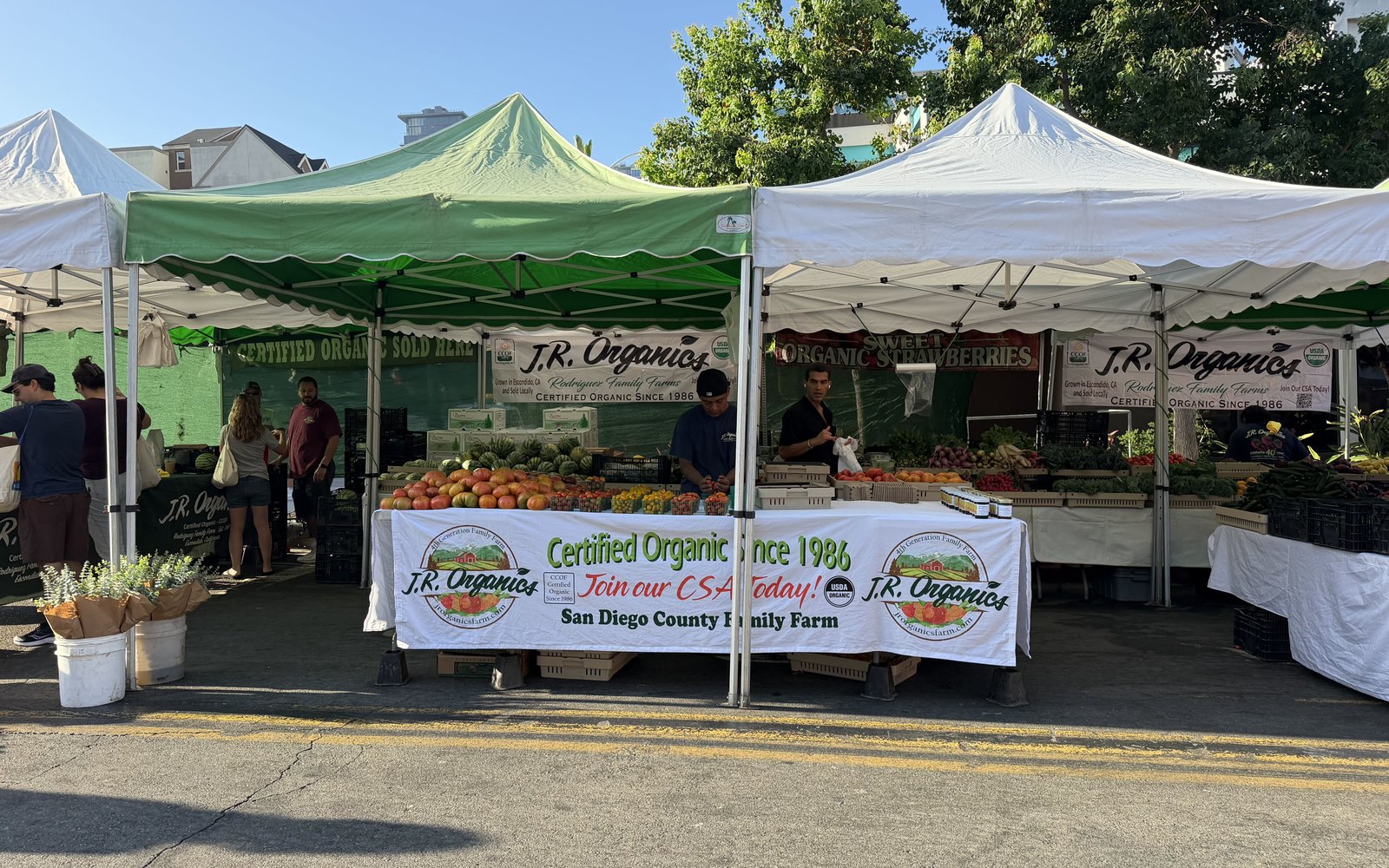 The JR Organics stand at market, its banner reading Certified Organic Since 1986 and Join our CSA Today