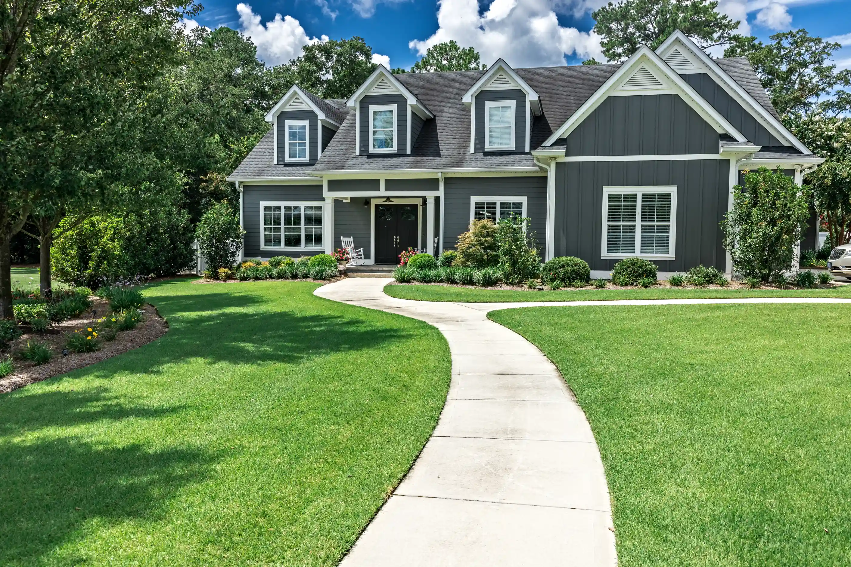 Elegant gray house exterior with dormer windows, porch and manicured lawn
