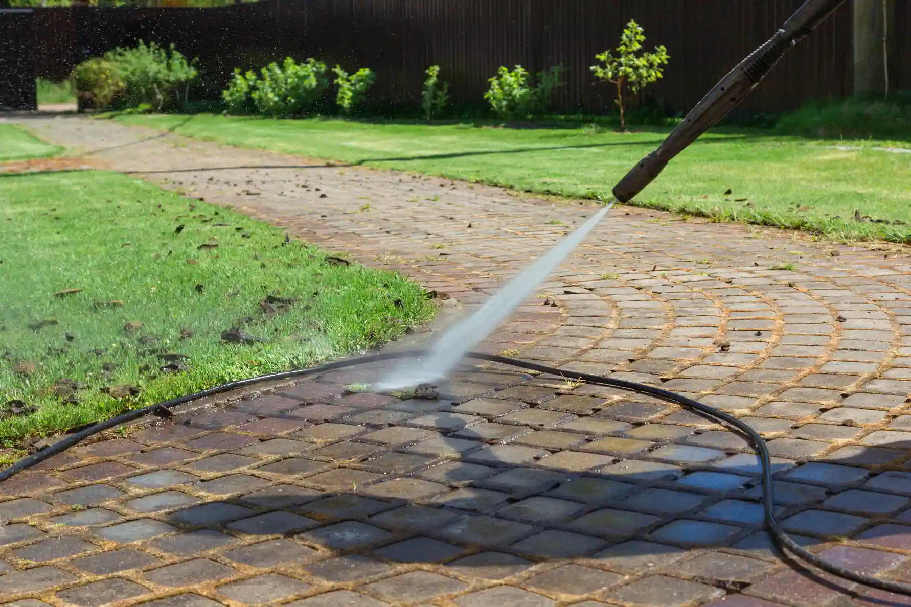 Pressure washer spraying water on brick patio, cleaning between pavers