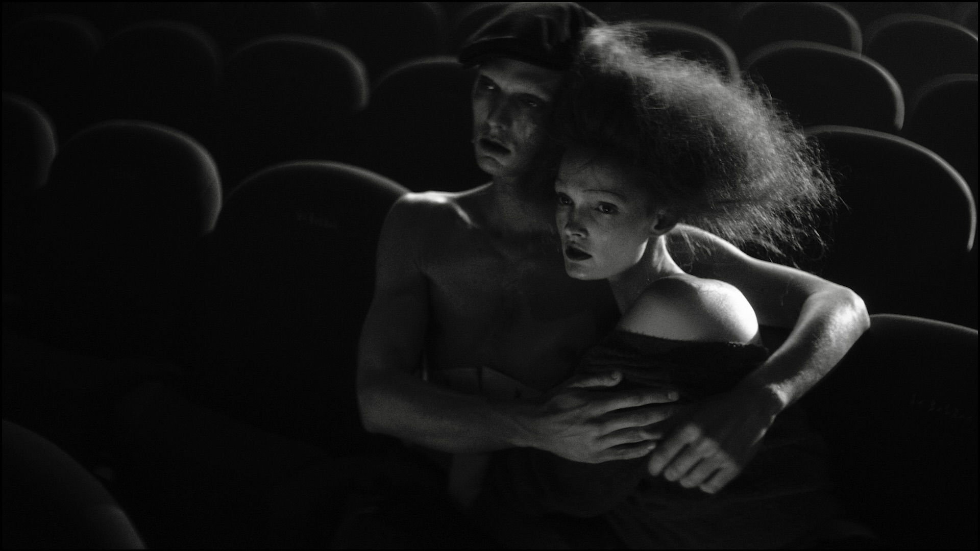 Two performers seated together in the cinema, in a monochrome close view.
