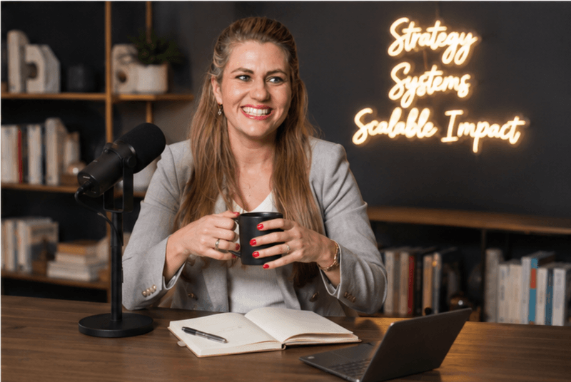 Mandy Hornaday in her content studio in front of a Strategy, Systems, Scalable Impact neon sign