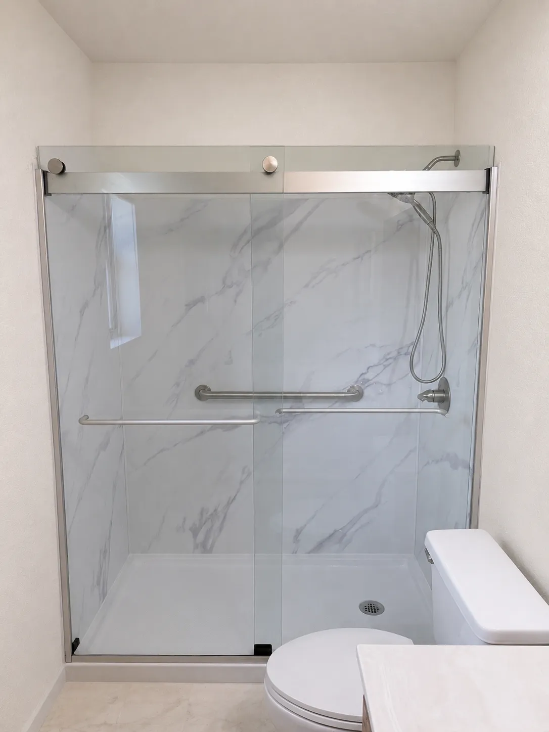 Finished walk-in shower with marble-look panels and sliding glass doors