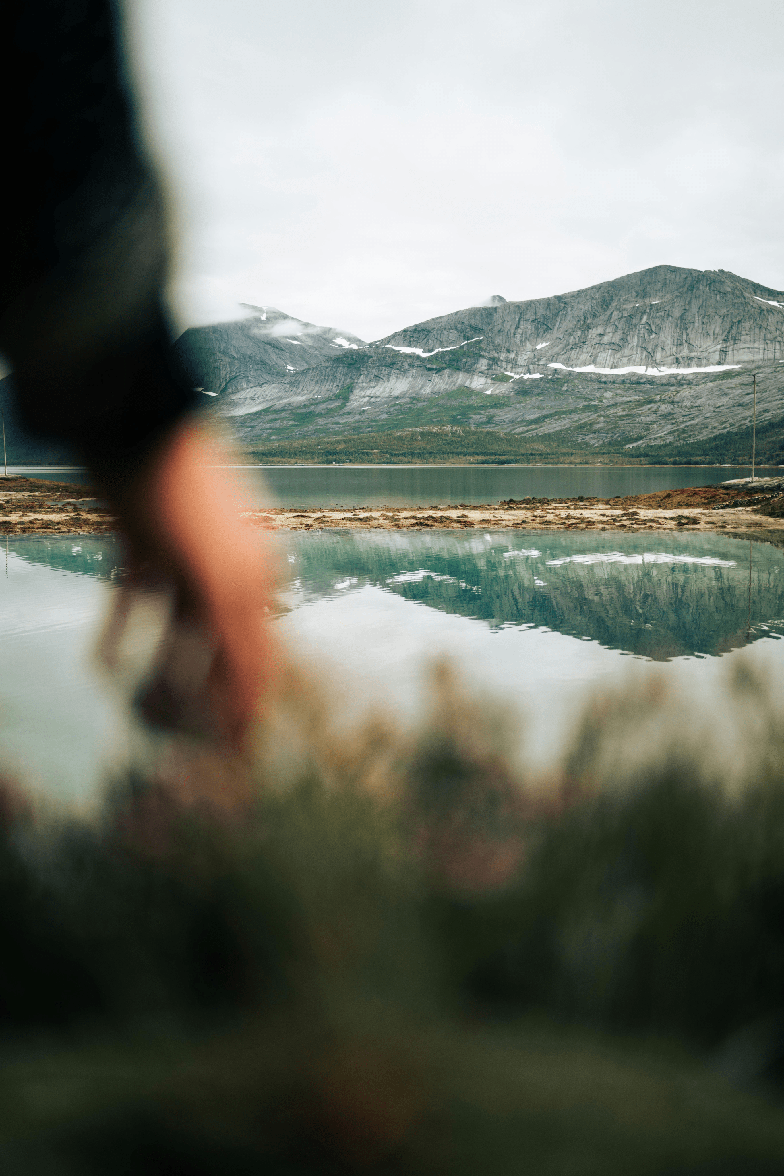 A calm Norwegian fjord below snow-streaked mountains, mirrored in still water