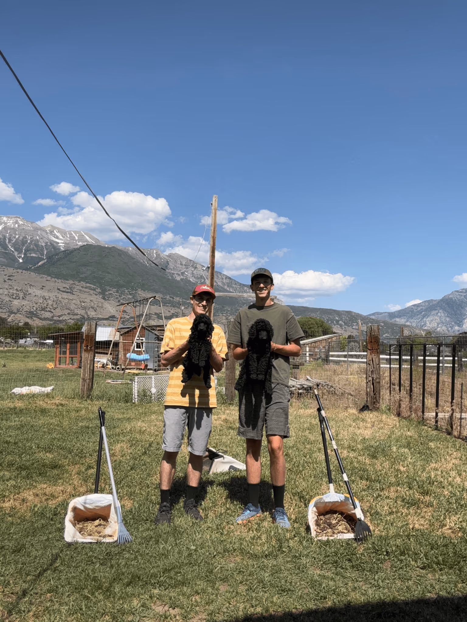 Spencer and AJ holding two poodle pups while standing next to their pooper scoopers