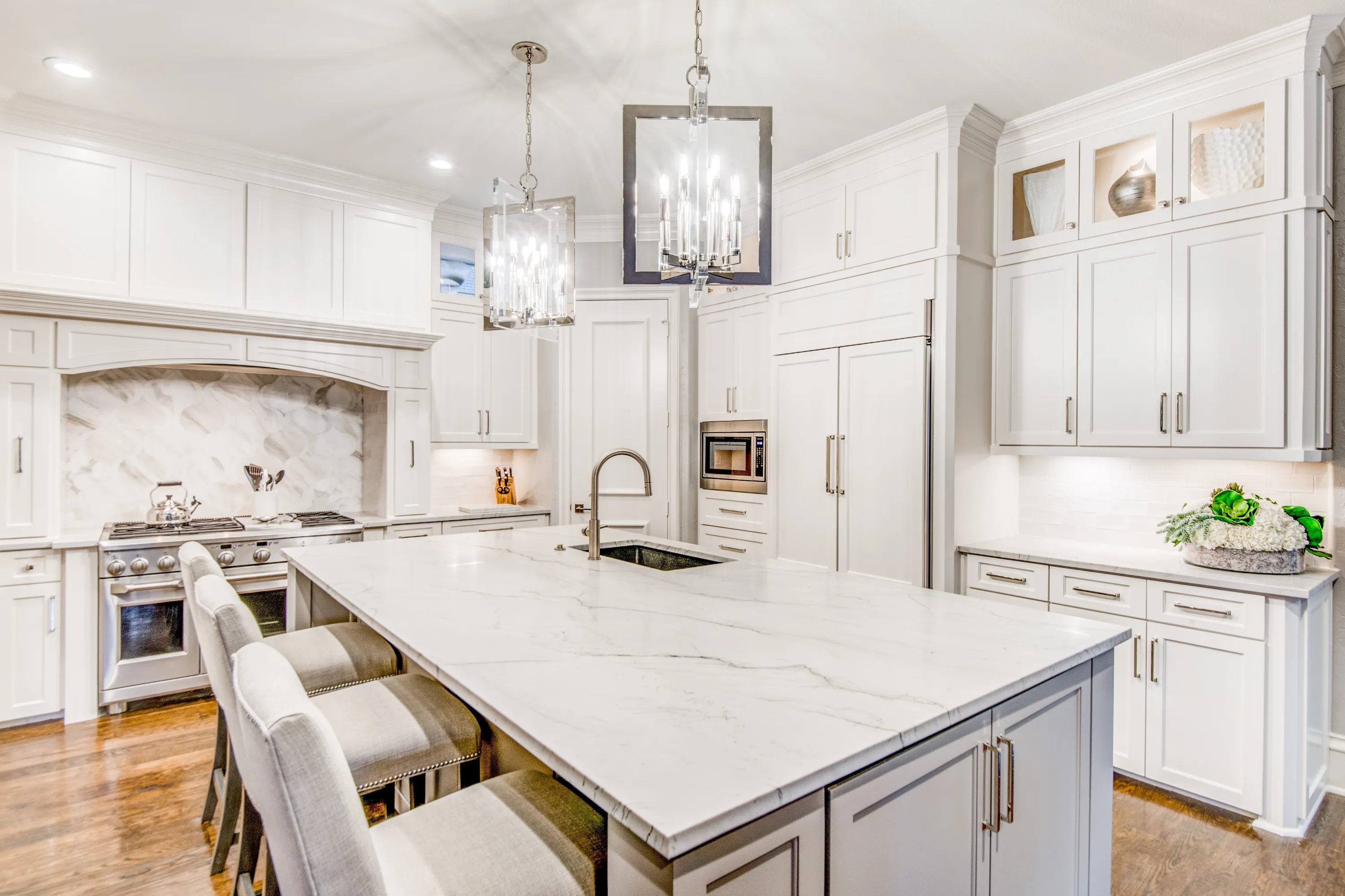 Bright kitchen with coordinated white cabinetry, a large island, pendant lights, and warm wood flooring