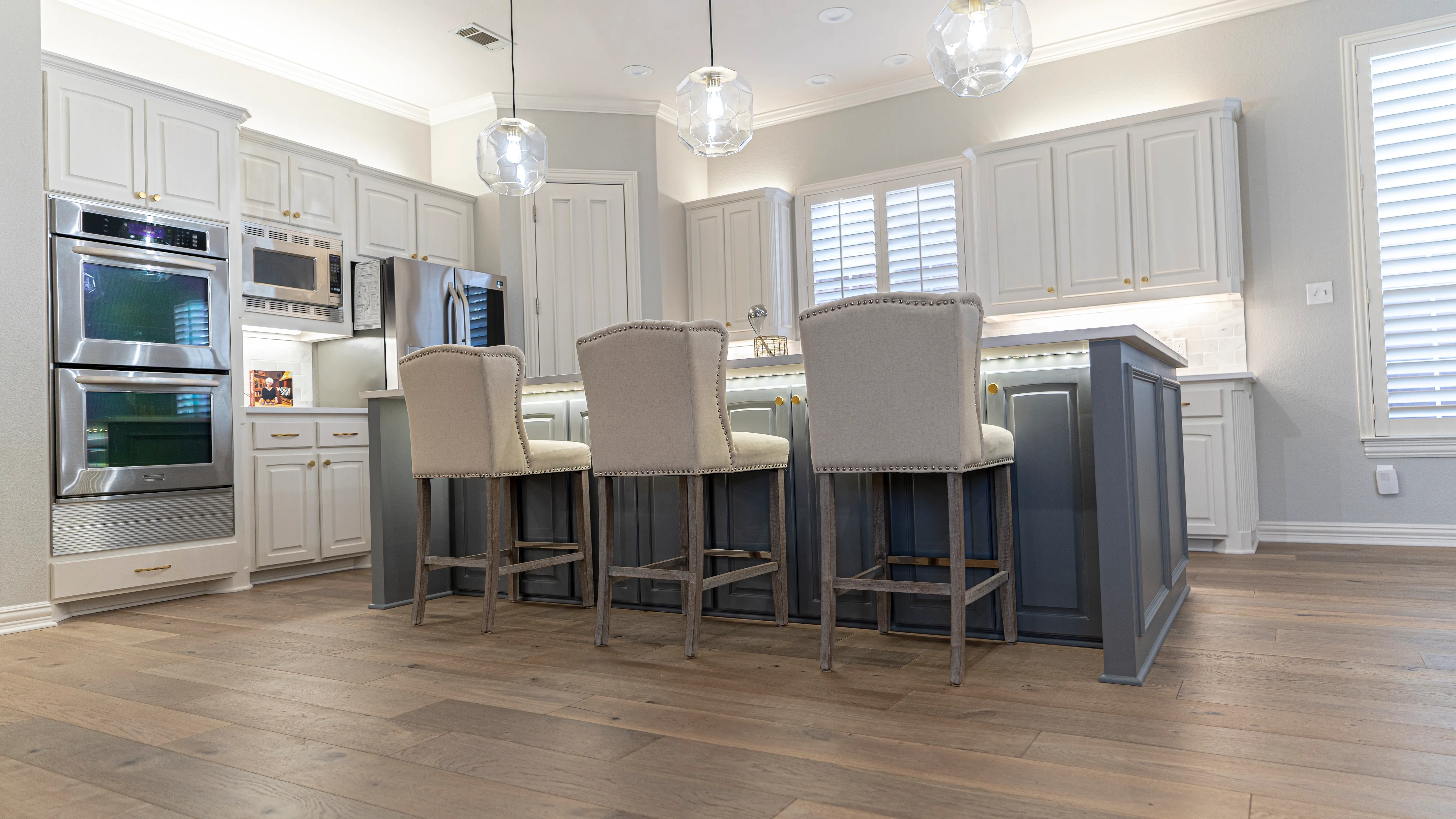 Warm wood-look plank flooring across a kitchen with white cabinets and a dark island
