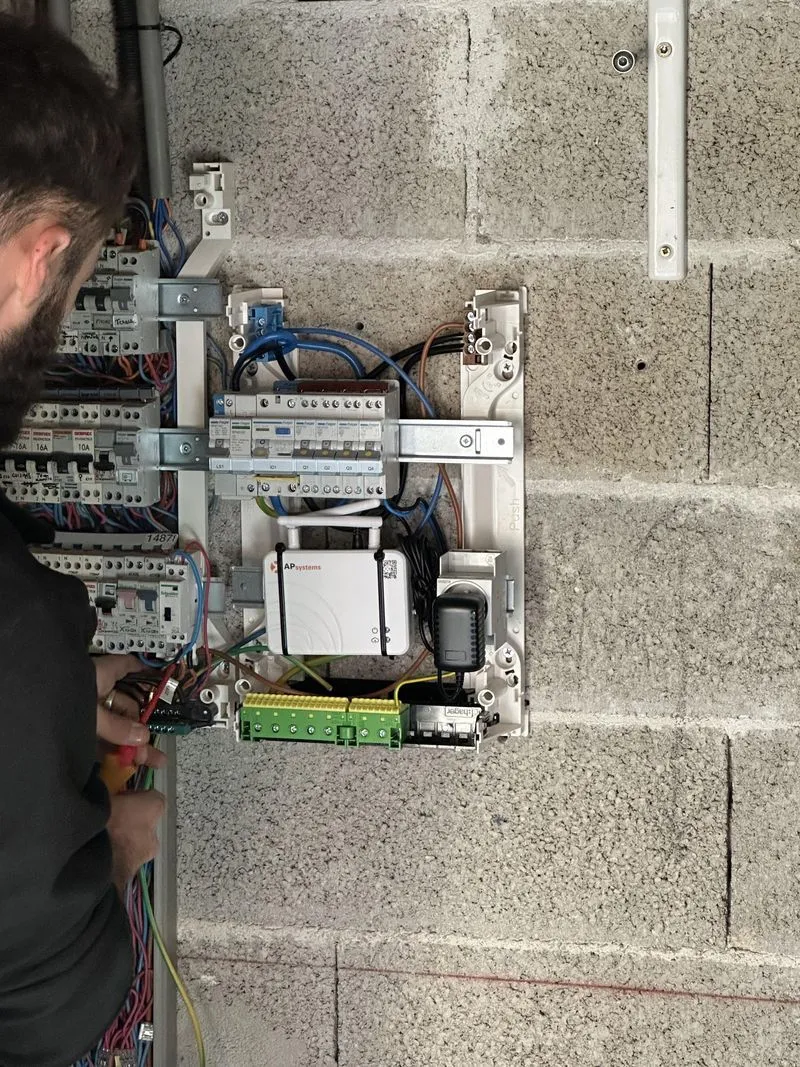 Électricien intervenant sur un tableau électrique ouvert avec une passerelle photovoltaïque.