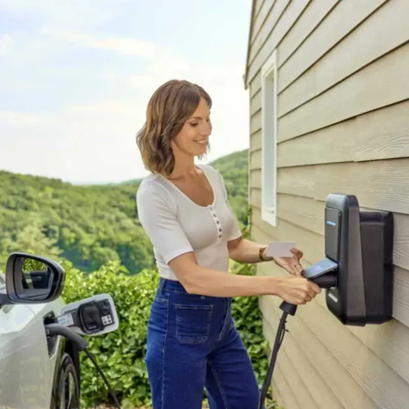 Personne manipulant le câble d’une borne de recharge murale près d’une voiture.